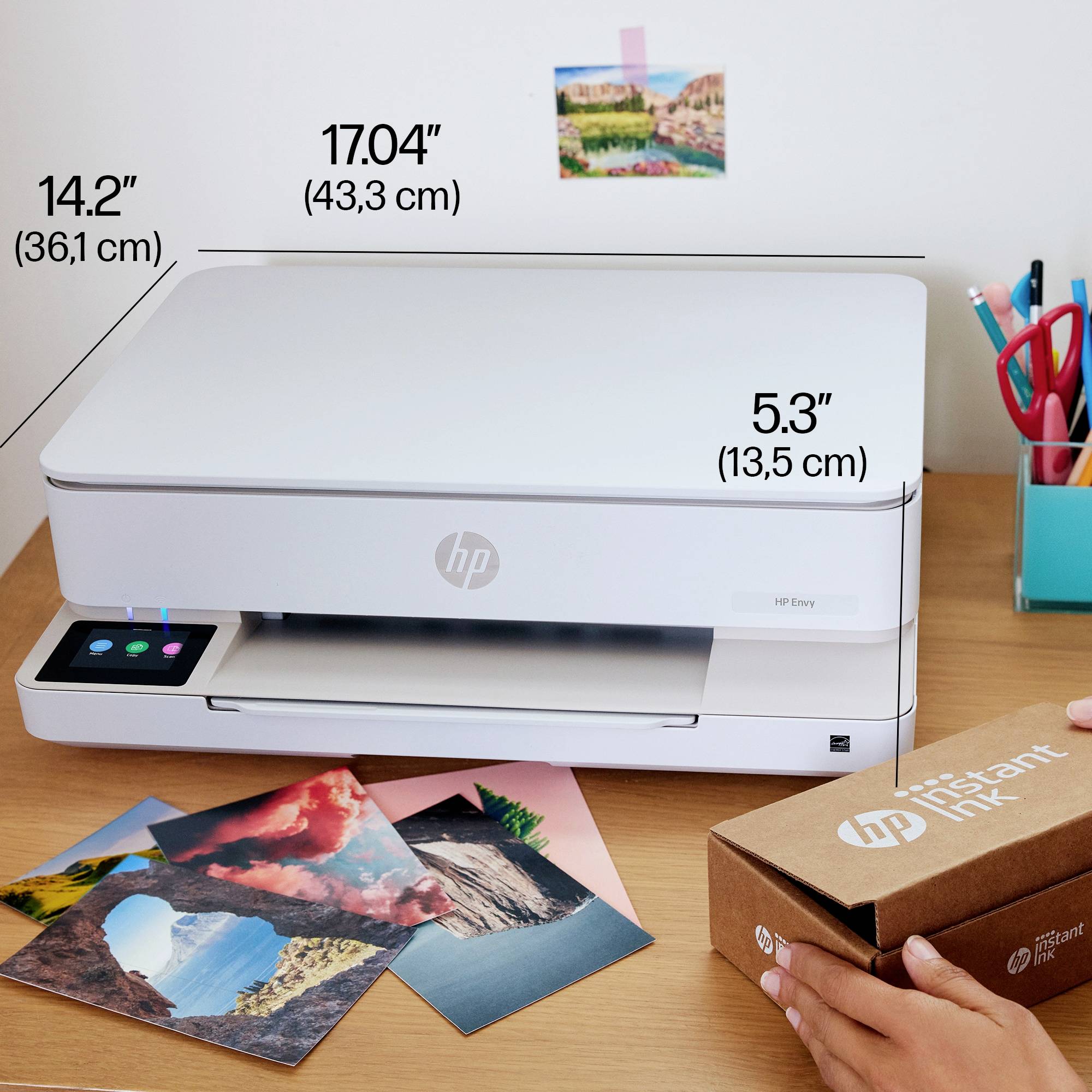 Printer on a table with photos and a box beside it. Dimensions: Width 17 inches (43.3 cm), Height 5.3 inches (13.5 cm), Depth 14.2 inches (36.1 cm).