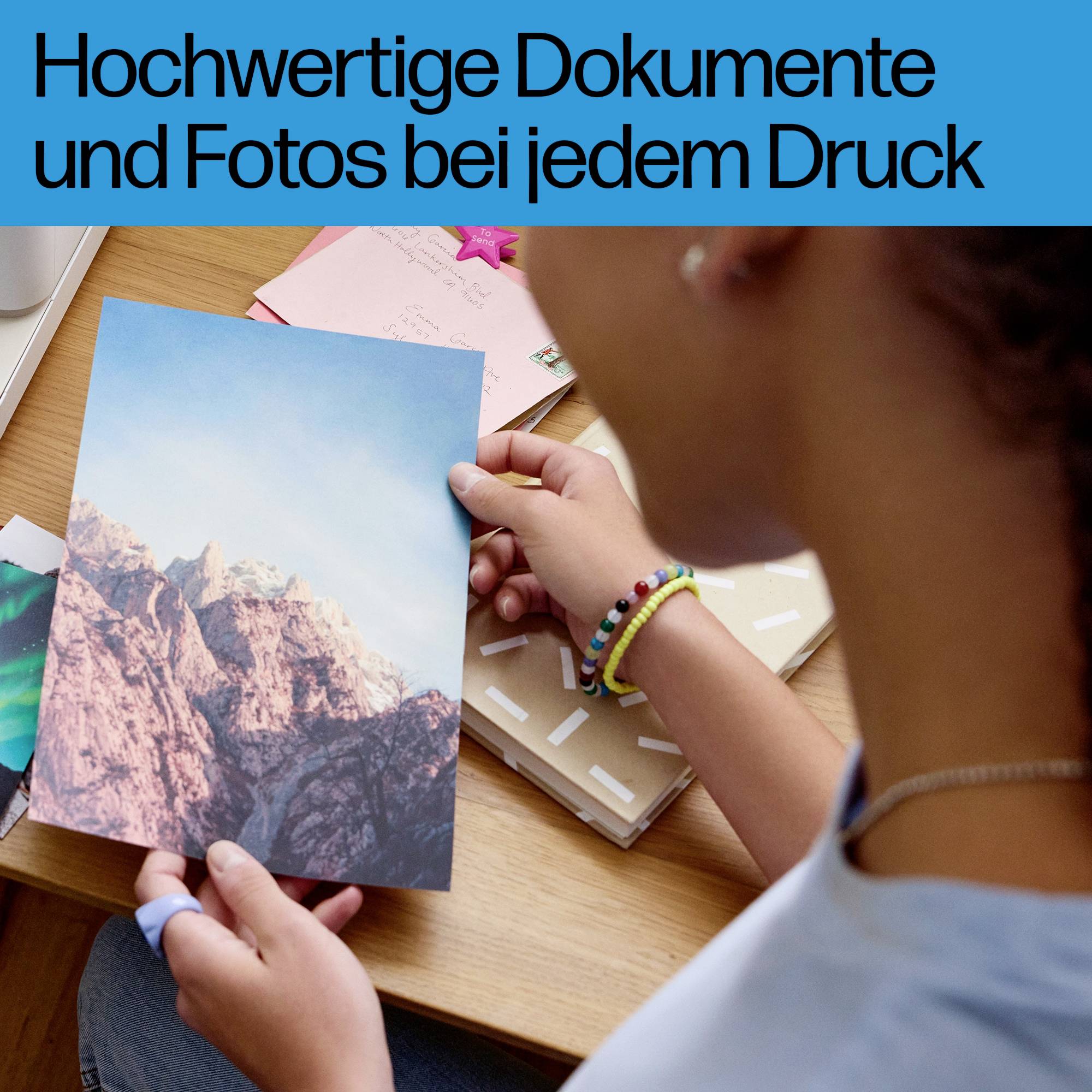 A person examines a photo, holding a print in their hand, with a notebook beside it on the desk. Text at the top: 'High-quality documents and photos with every print'.