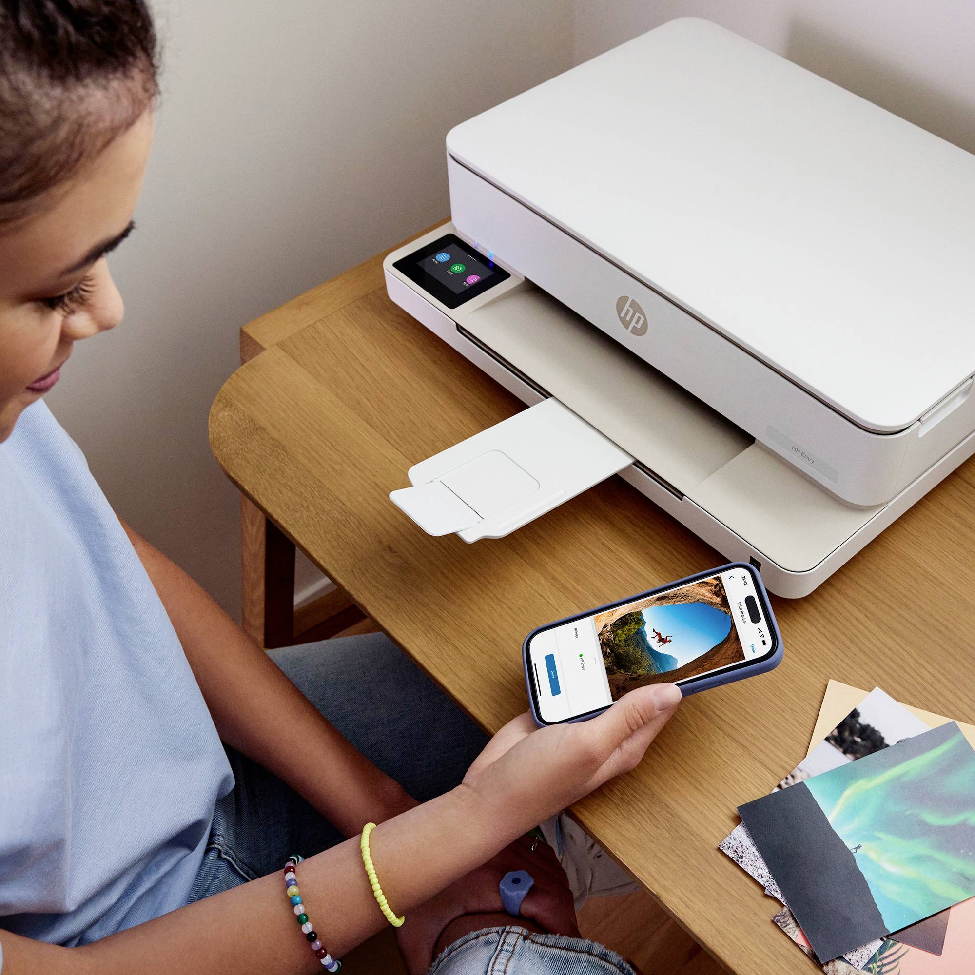 A person is using a smartphone to send a photo directly to a printer. The printer is on a wooden table.
