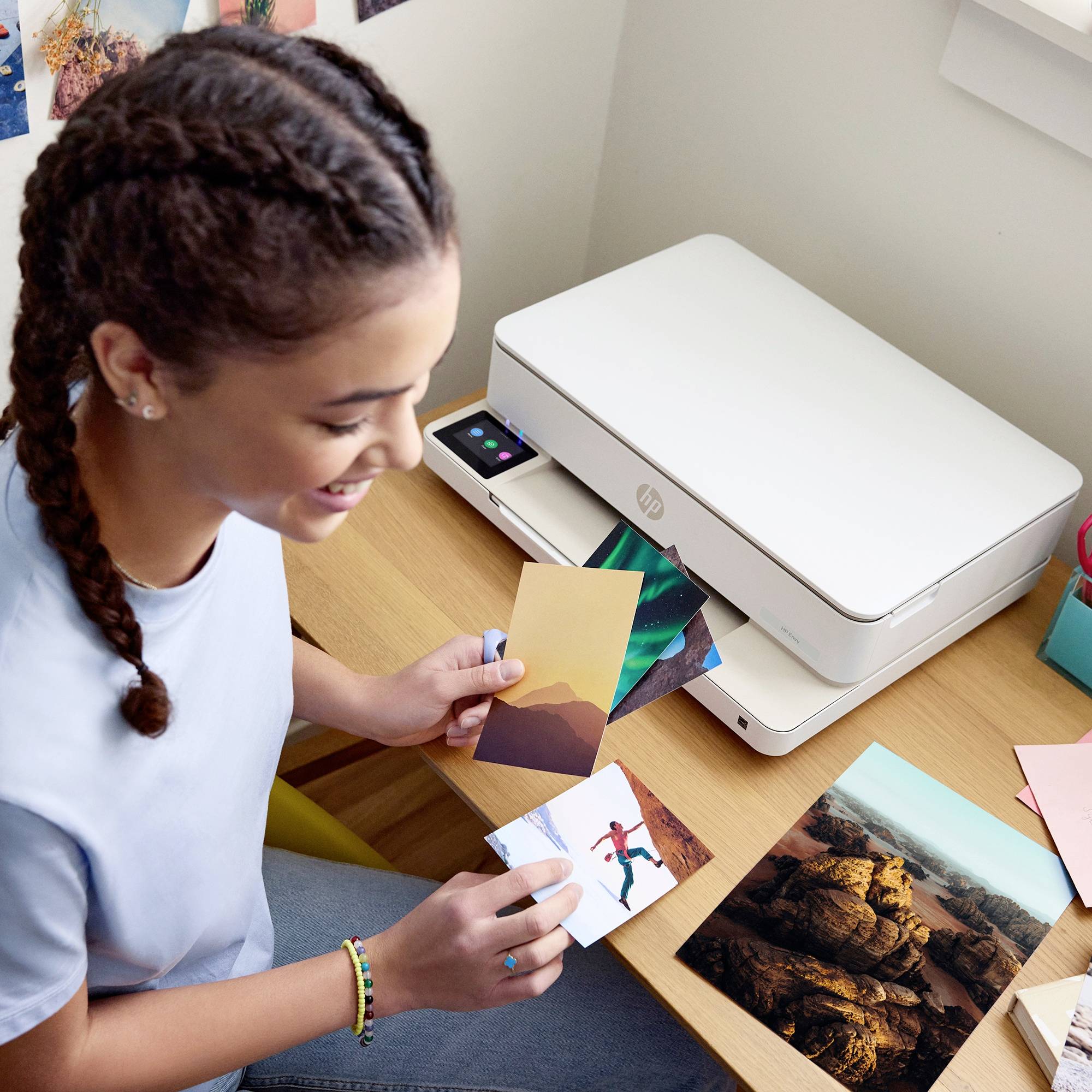 A person with braided hair is smiling while sorting photographs next to a printer. More photos can be seen in the background.