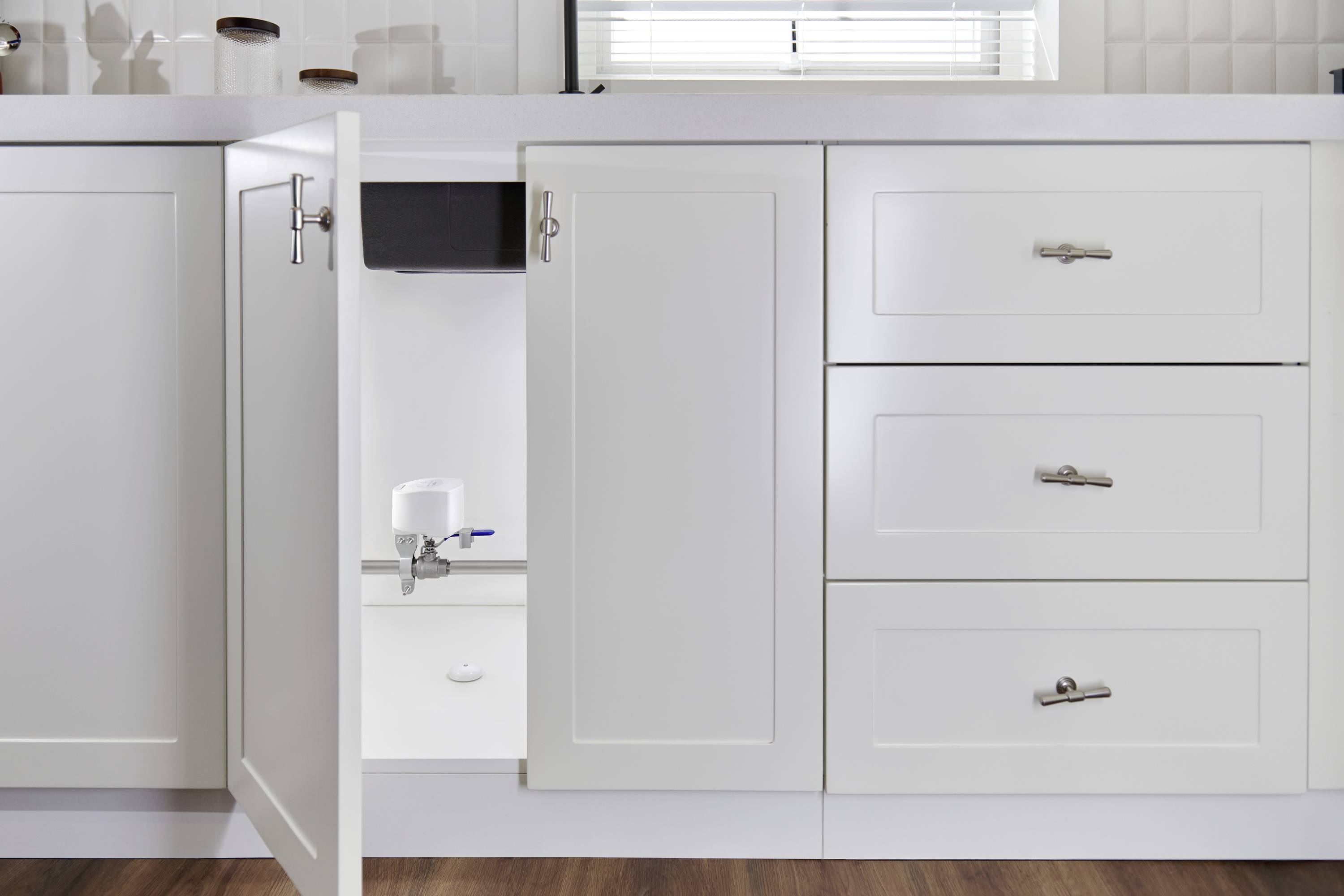 An open kitchen cupboard reveals a water filtration system installed beneath the sink. Simple, modern design.