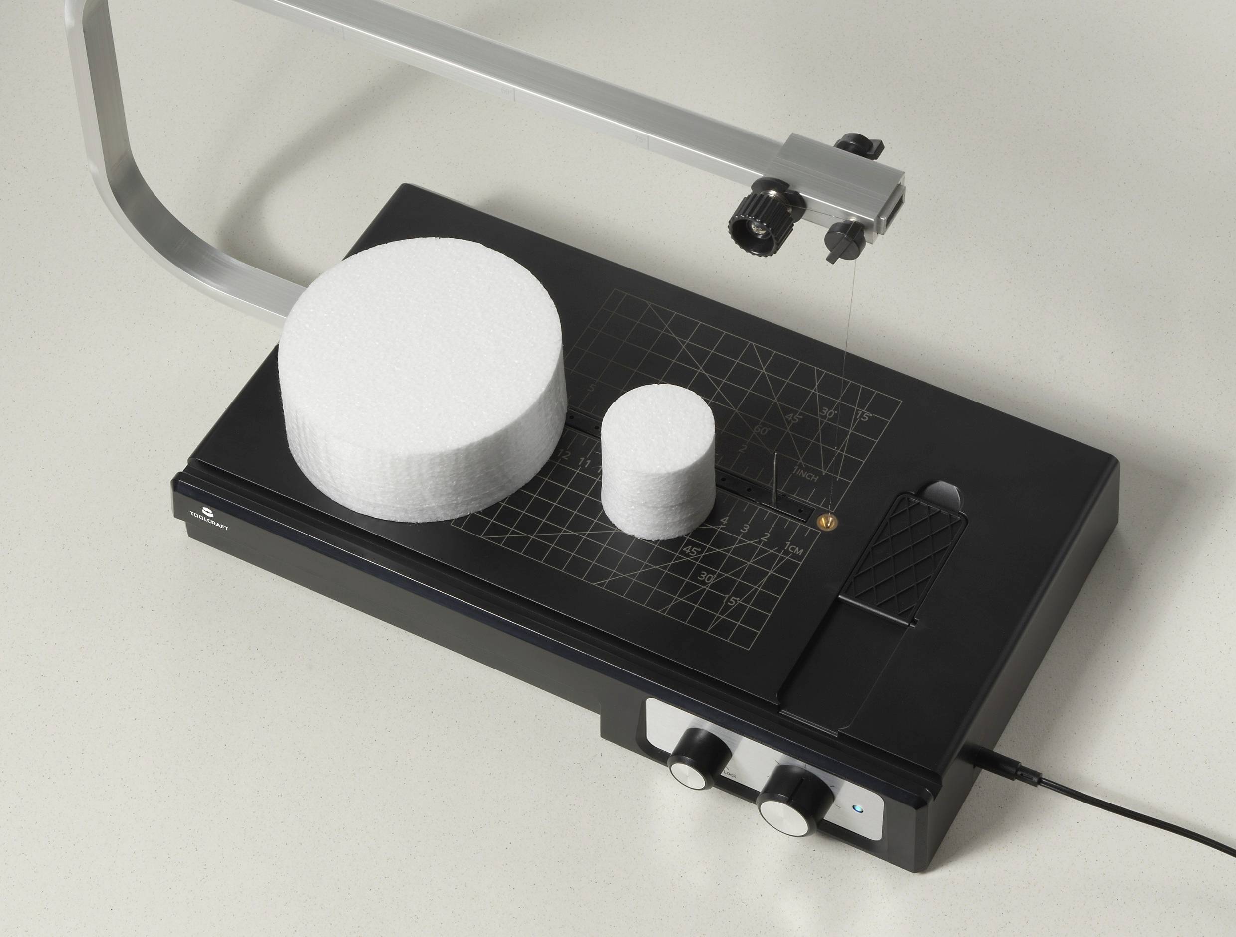 Electric polystyrene cutting machine with two white, round polystyrene blocks placed on top. Device is powered via a mains plug.