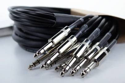 A bundle of audio cables with multiple jack plugs in various sizes, lying on a white surface.