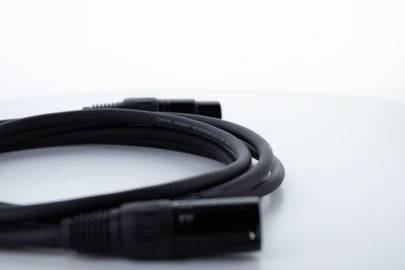 A black audio cable with two XLR connectors lies on a white surface. It symbolises the connection in audio equipment.