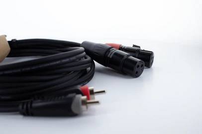 A coiled audio cable with XLR and RCA connectors lies on a table. Suitable for audio connections in recording studios.