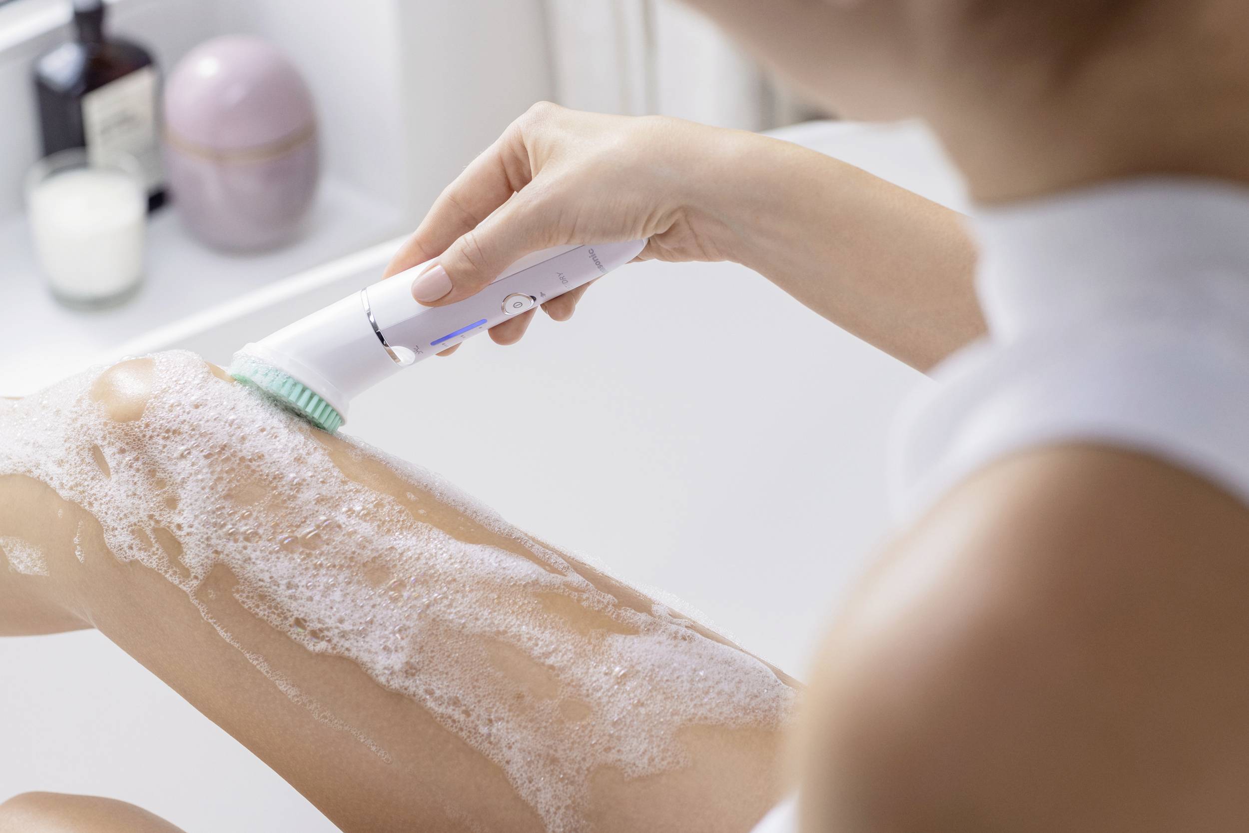 A person is cleaning a soapy leg with an electric brush in the bathroom.