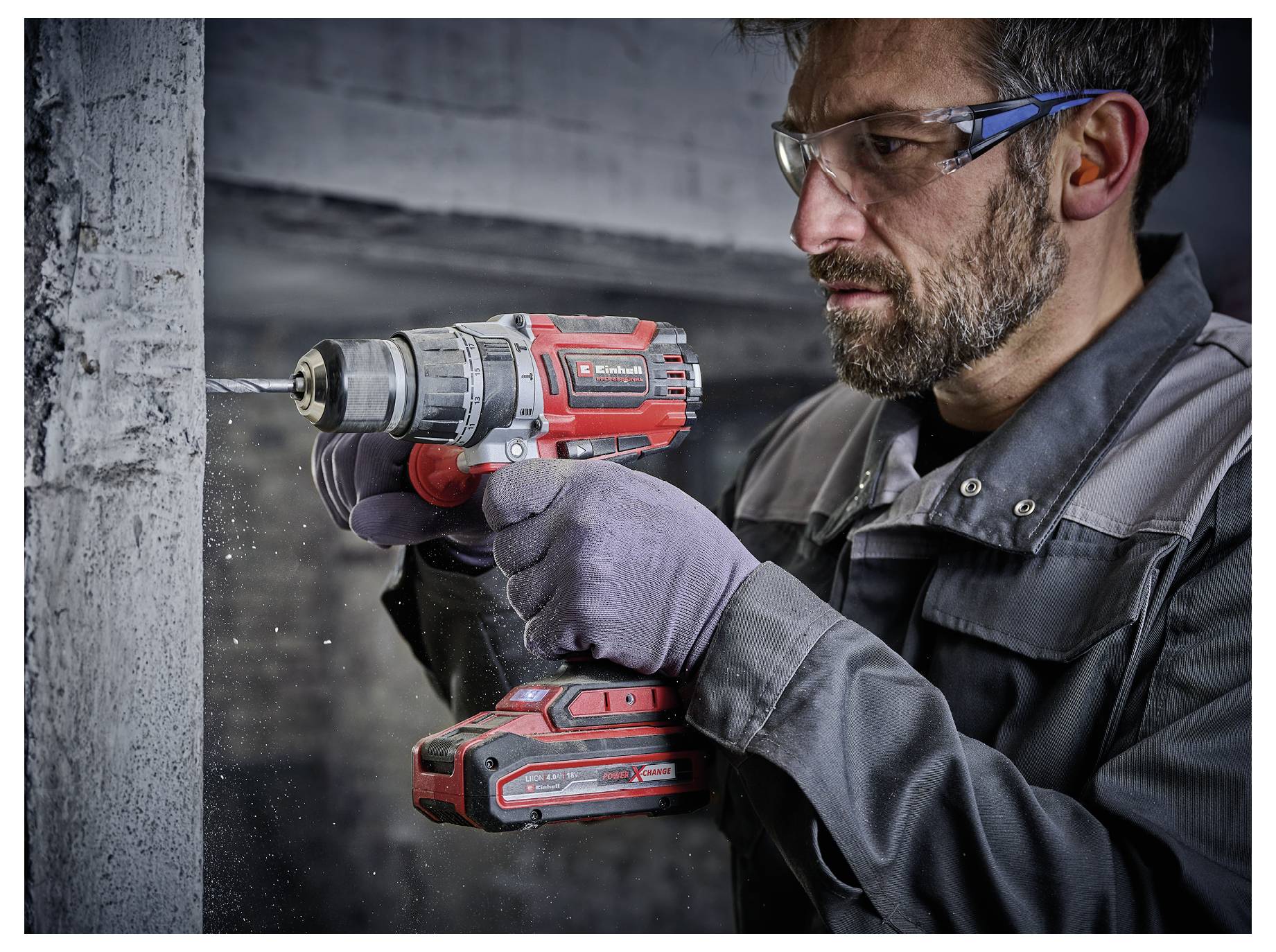 A person wearing protective eyewear and gloves uses a red and black power drill on a concrete surface, focusing intently on the task.