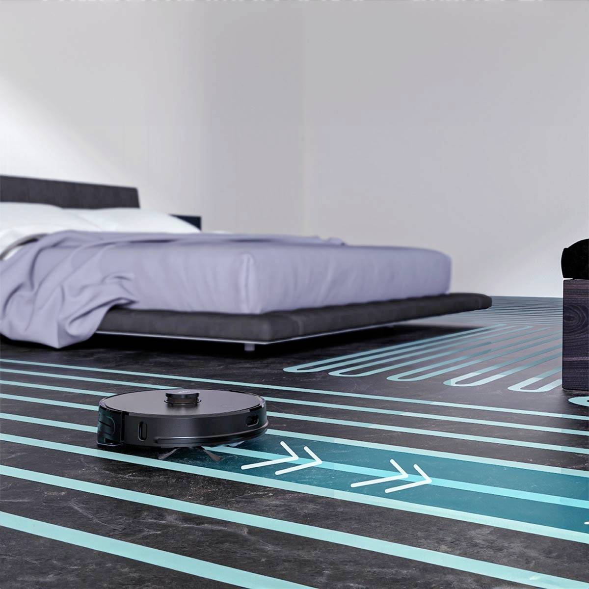 A robot vacuum cleaner is cleaning the floor in a modern bedroom. The bed is on an elevated frame, and the floor has a striped pattern.