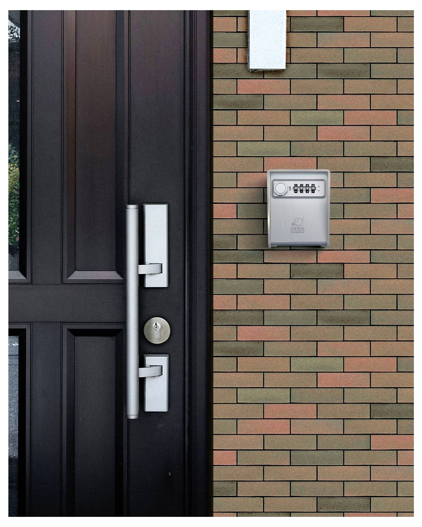 A black door with a silver handle next to a brick wall featuring a numeric keypad lockbox, indicating a secure entry system.