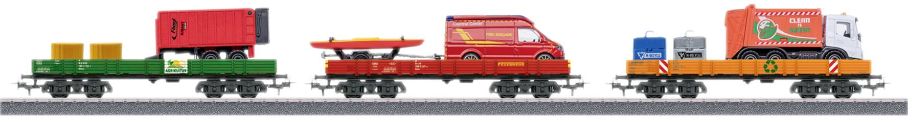 A model train with various goods wagons, loaded with containers, a boat, and a delivery van, on a railway track.