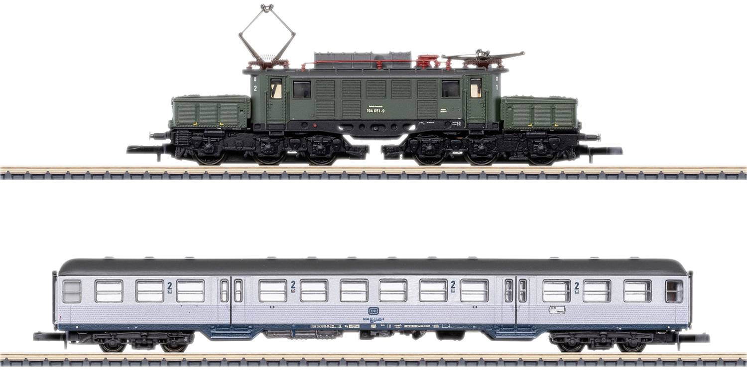 Two model railway trains on tracks: On top, a green locomotive with a pantograph; below, a silver passenger carriage.