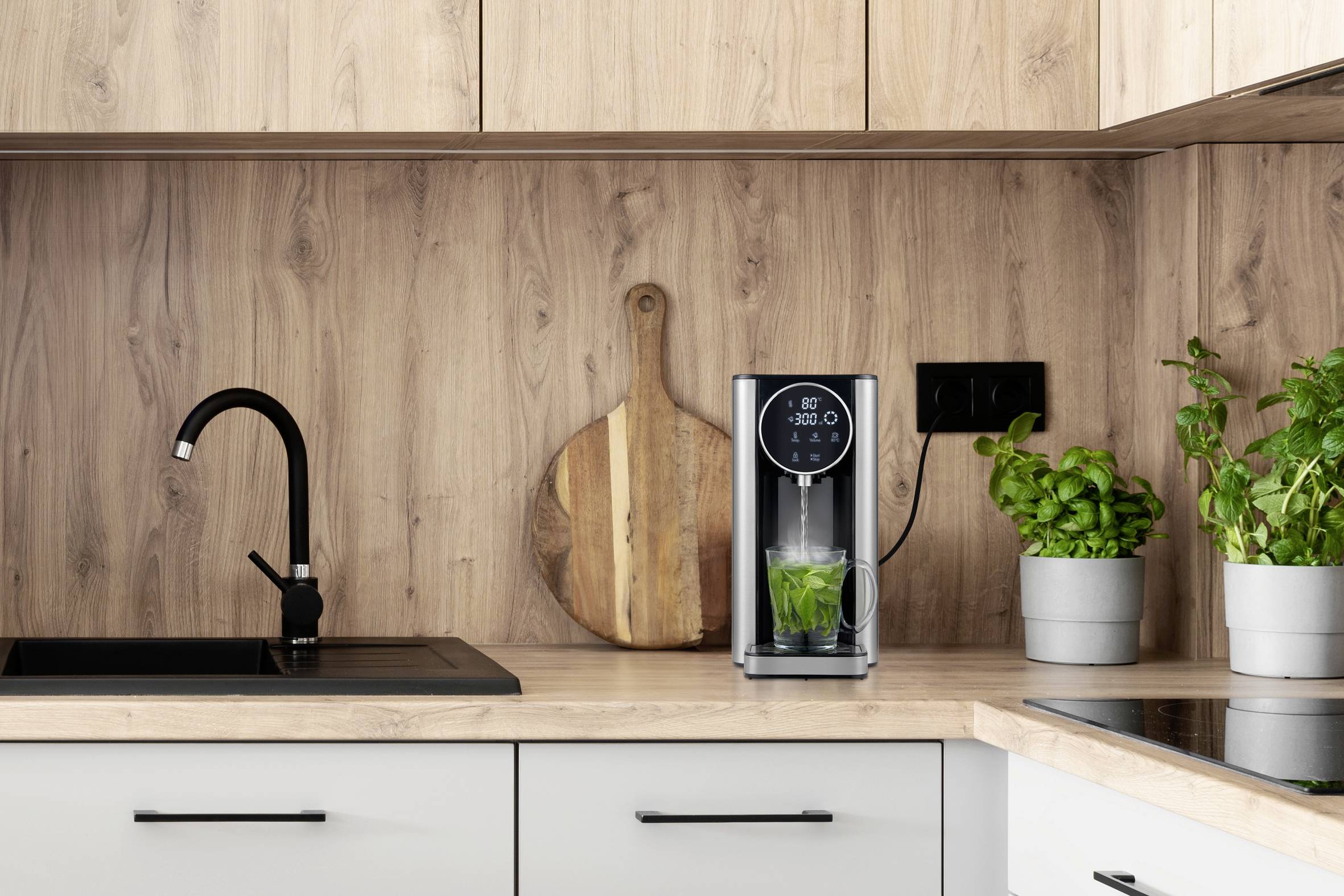 Kitchen worktop with a sparkling water dispenser, basil plants in pots beside it, and a wooden chopping board mounted on the wooden splashback.