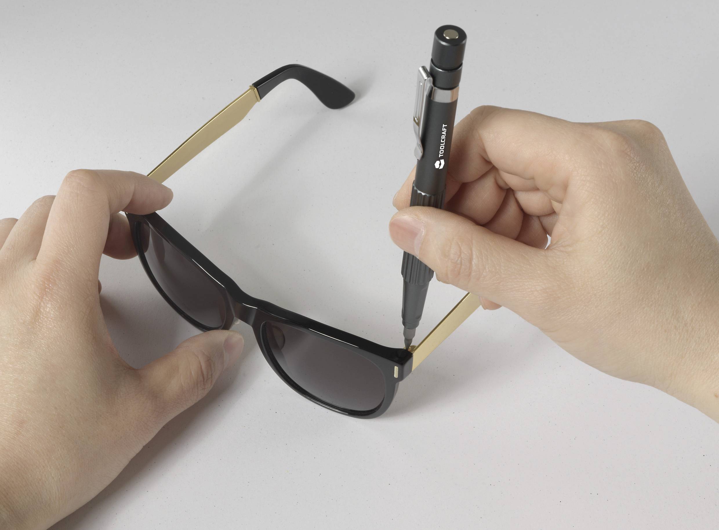 A person is repairing a pair of sunglasses with a small screwdriver.