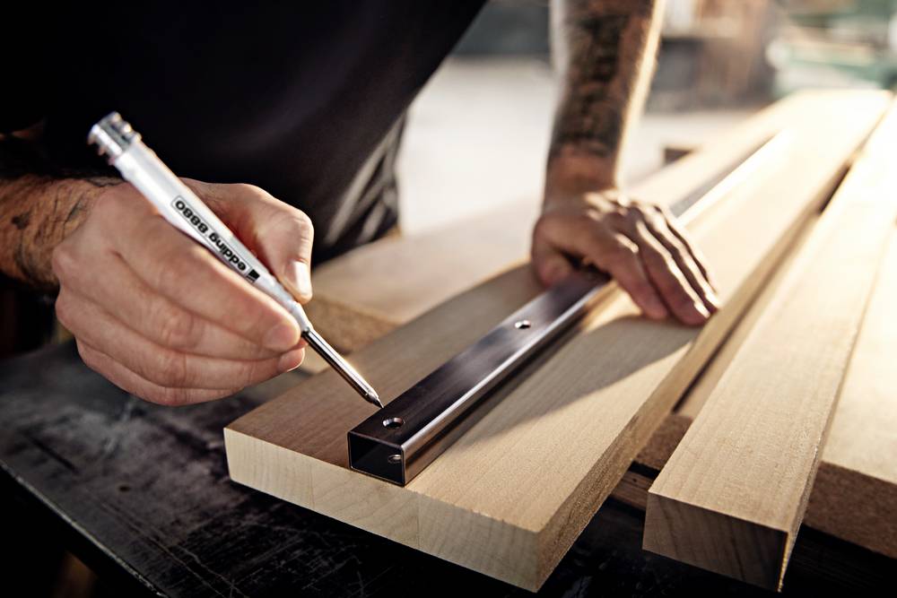 A person is measuring with a ruler and marking wooden boards on a workbench to prepare precise cuts.