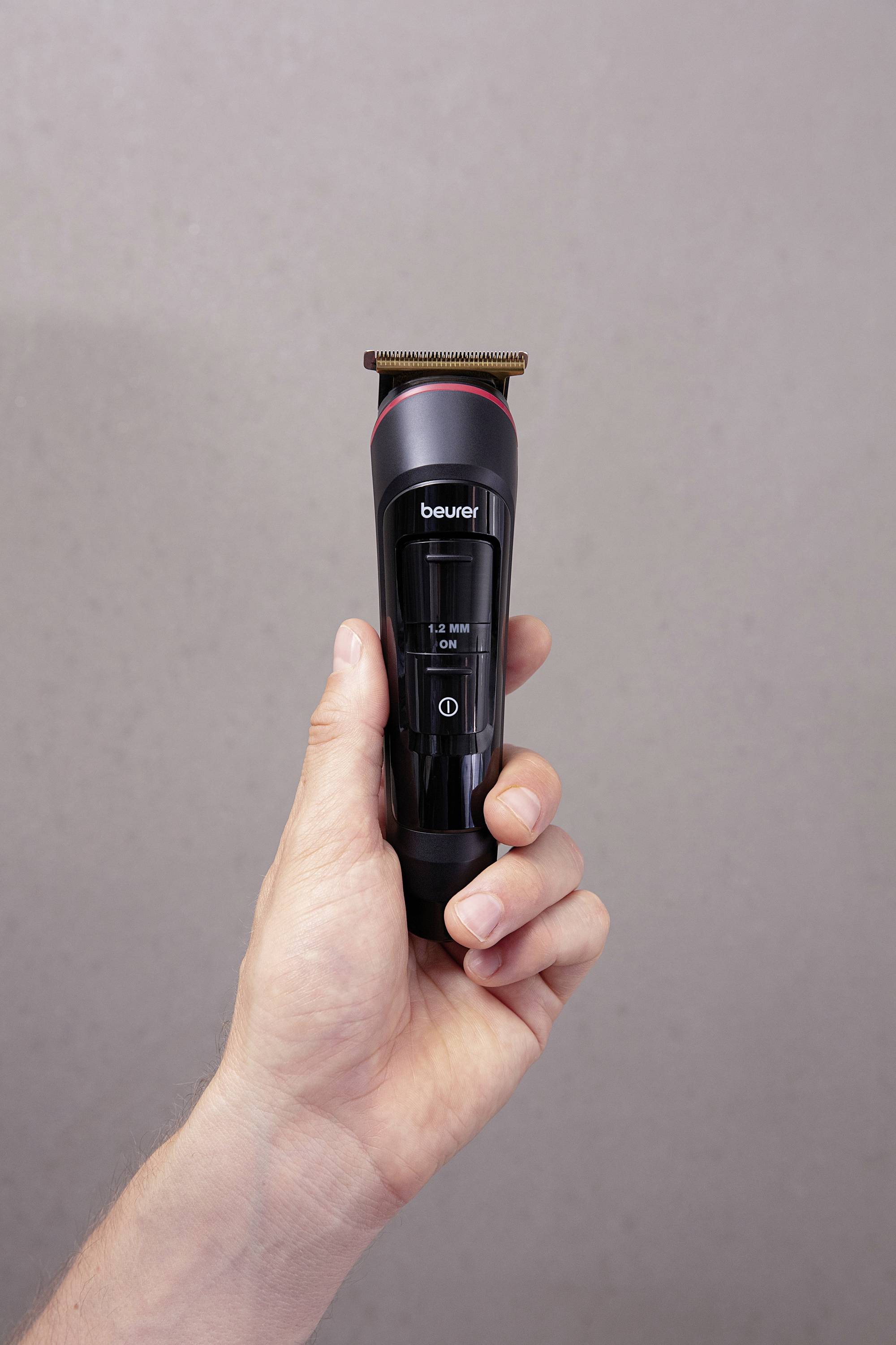 A hand is holding a black electric razor against a light grey background.