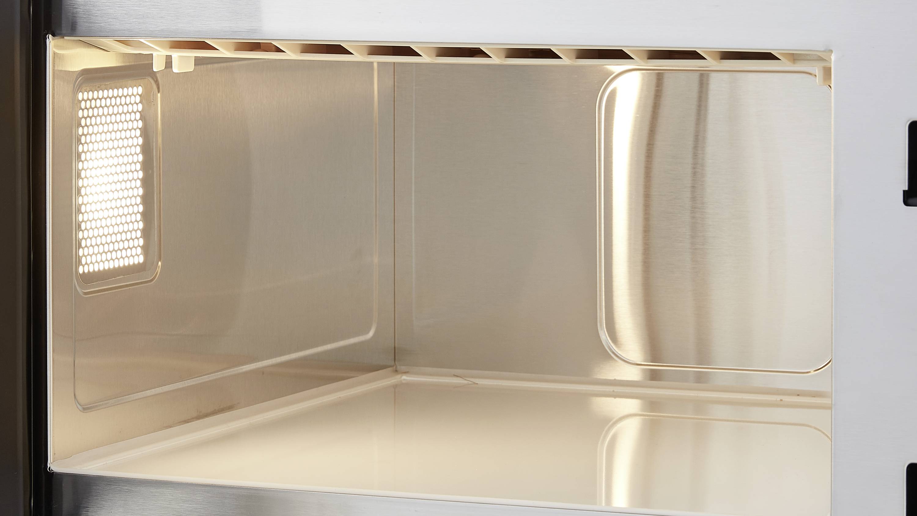 Metallic interior of an open microwave with lighting, showing an empty, clean surface.