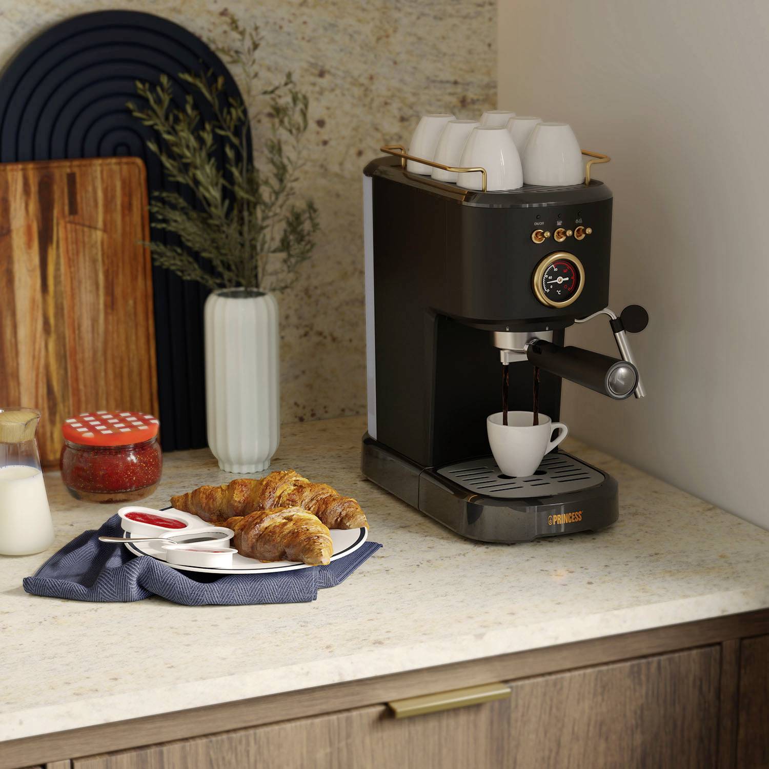 Table with coffee machine, cups, croissants on a plate and jam. Milk jug and green branch in the background.