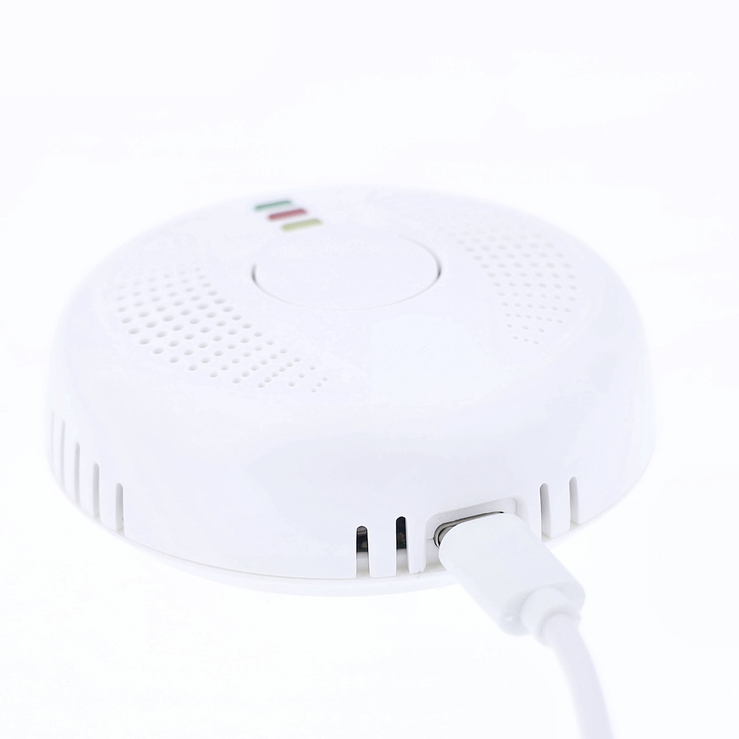 A white smoke detector with an attached cable, showing red, green, and yellow LEDs as function indicators.