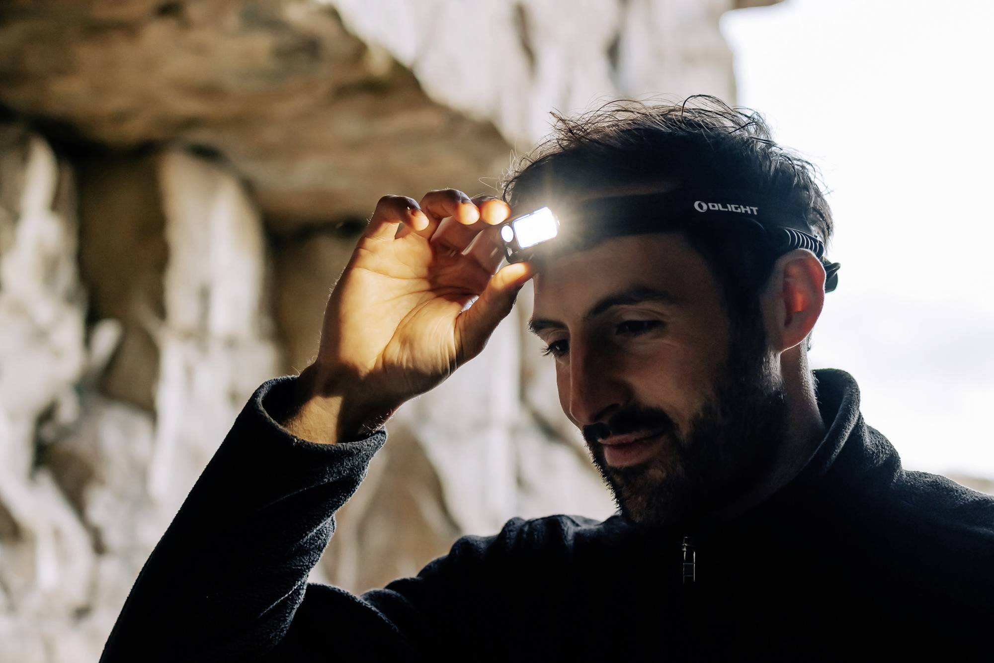 A person is wearing a head torch in a cave, illuminating their face with soft light in order to see the surroundings better.