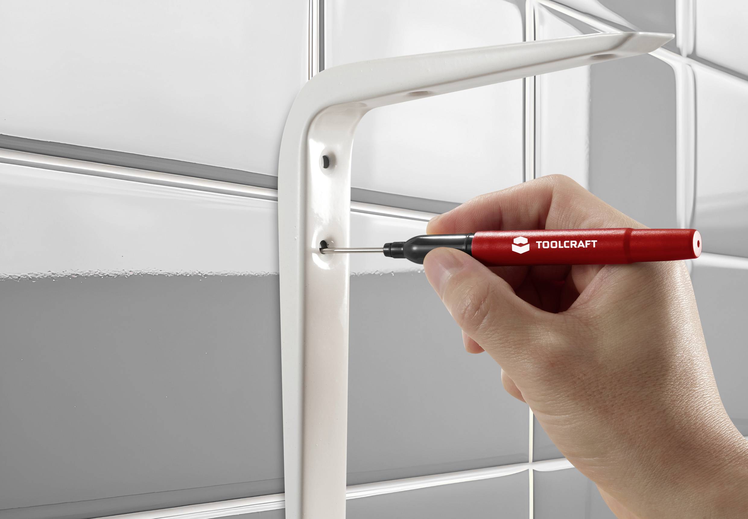 A hand is holding a red TOOLCRAFT screwdriver and tightening a screw in a white bracket to secure it to the wall.