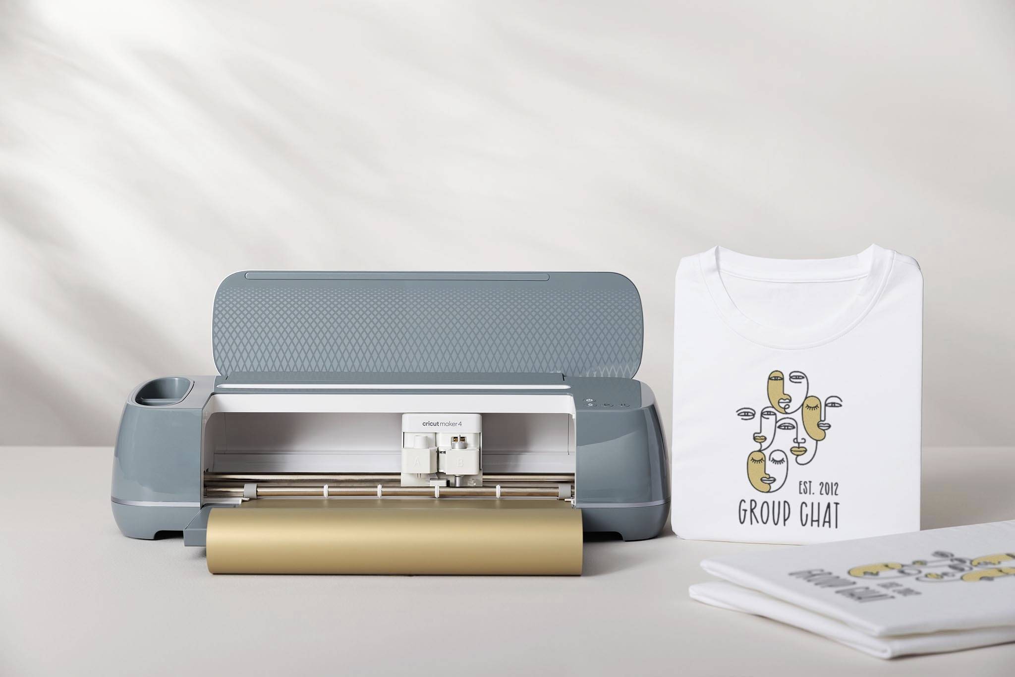 A cutting plotter on a table next to a T-shirt with a design and a stack of paper.
