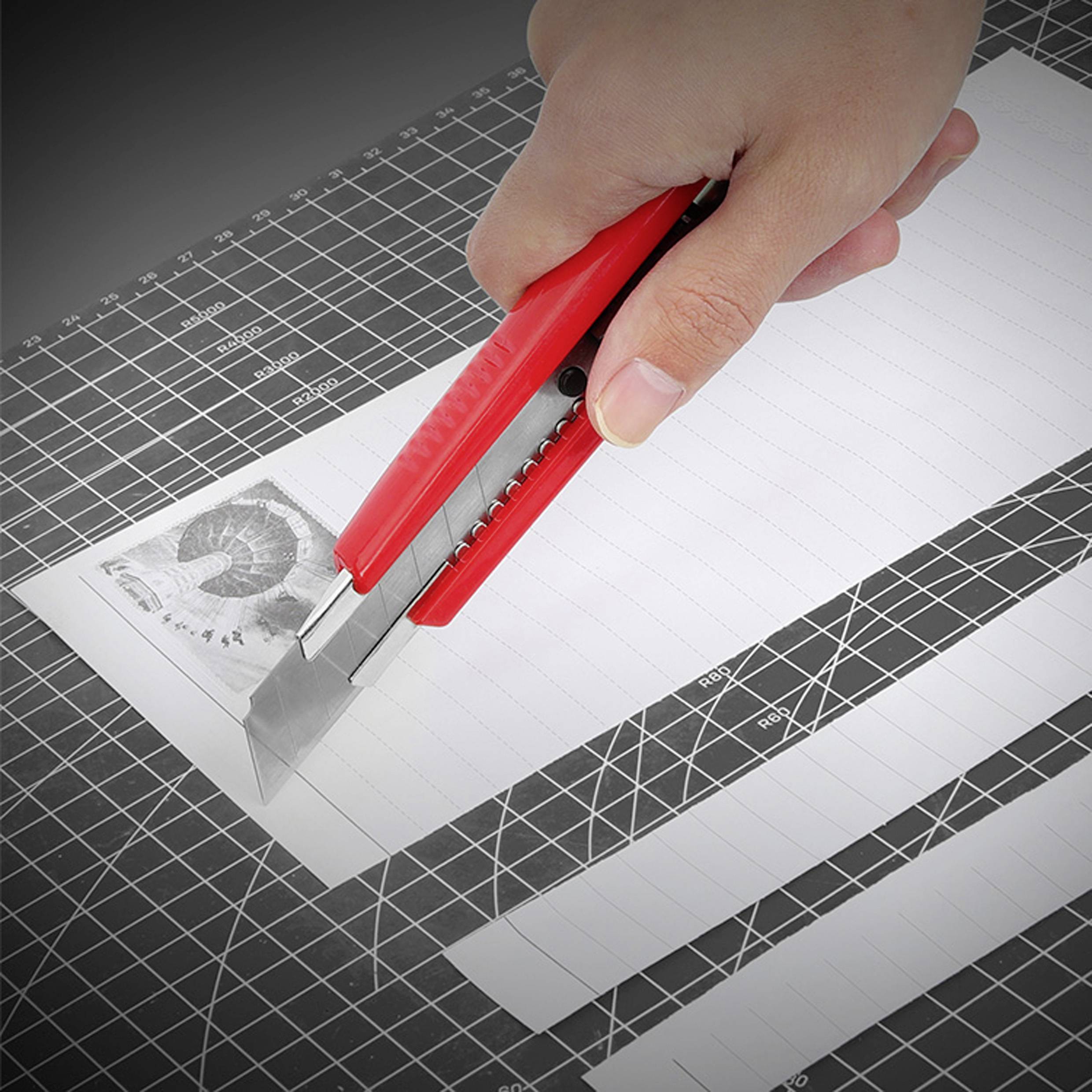 A hand is cutting white striped paper with a red craft knife on a cutting mat.