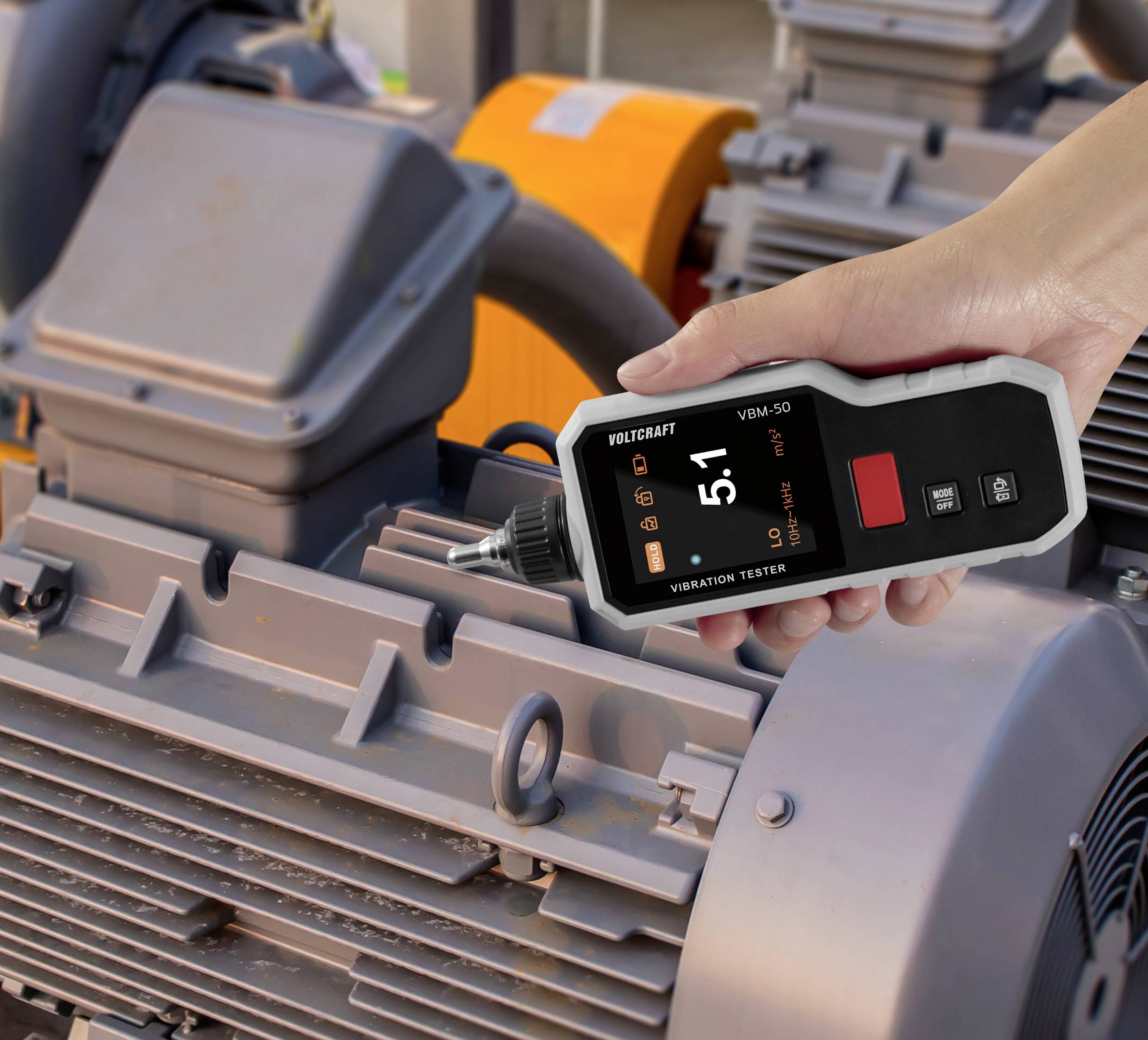 A person is using a handheld vibration tester on industrial machinery, displaying a reading of '5.1'.