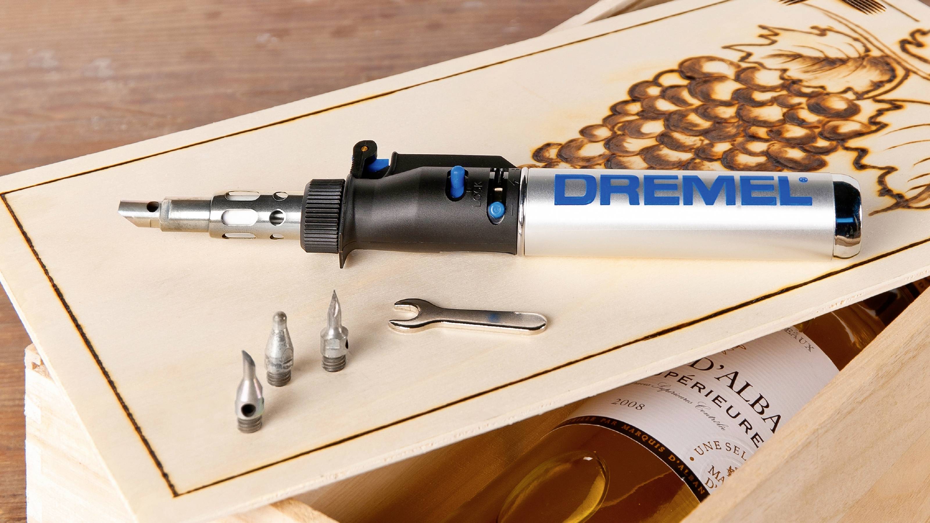 A Dremel tool lies on a wooden crate with a wine-themed design, surrounded by accessories and a small spanner.