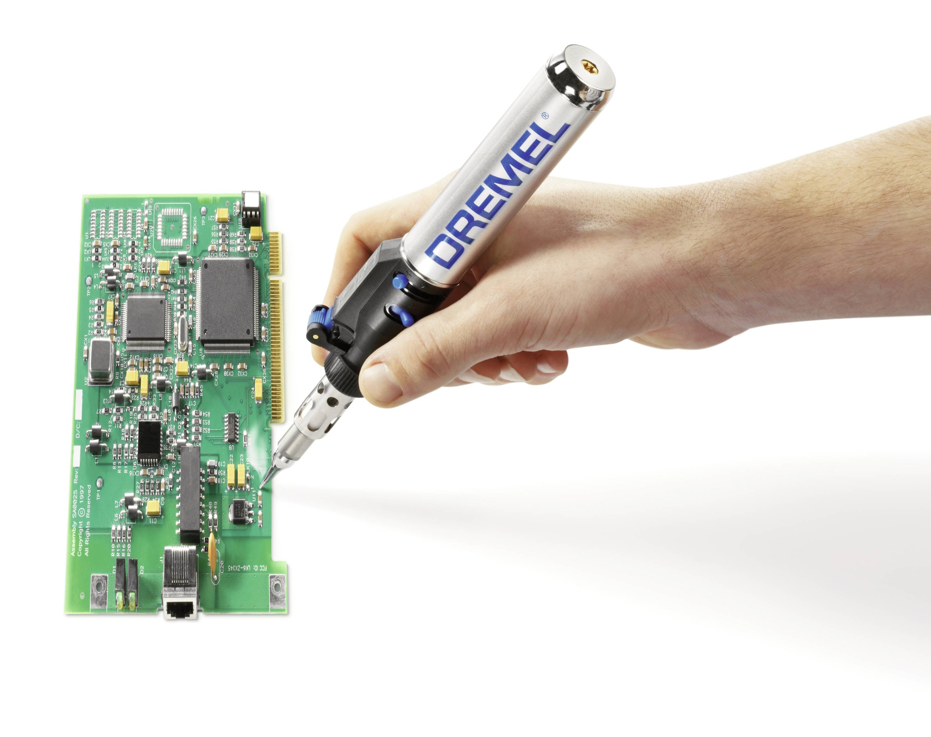 Close-up of a hand working with a Dremel tool on a green circuit board with various electronic components.