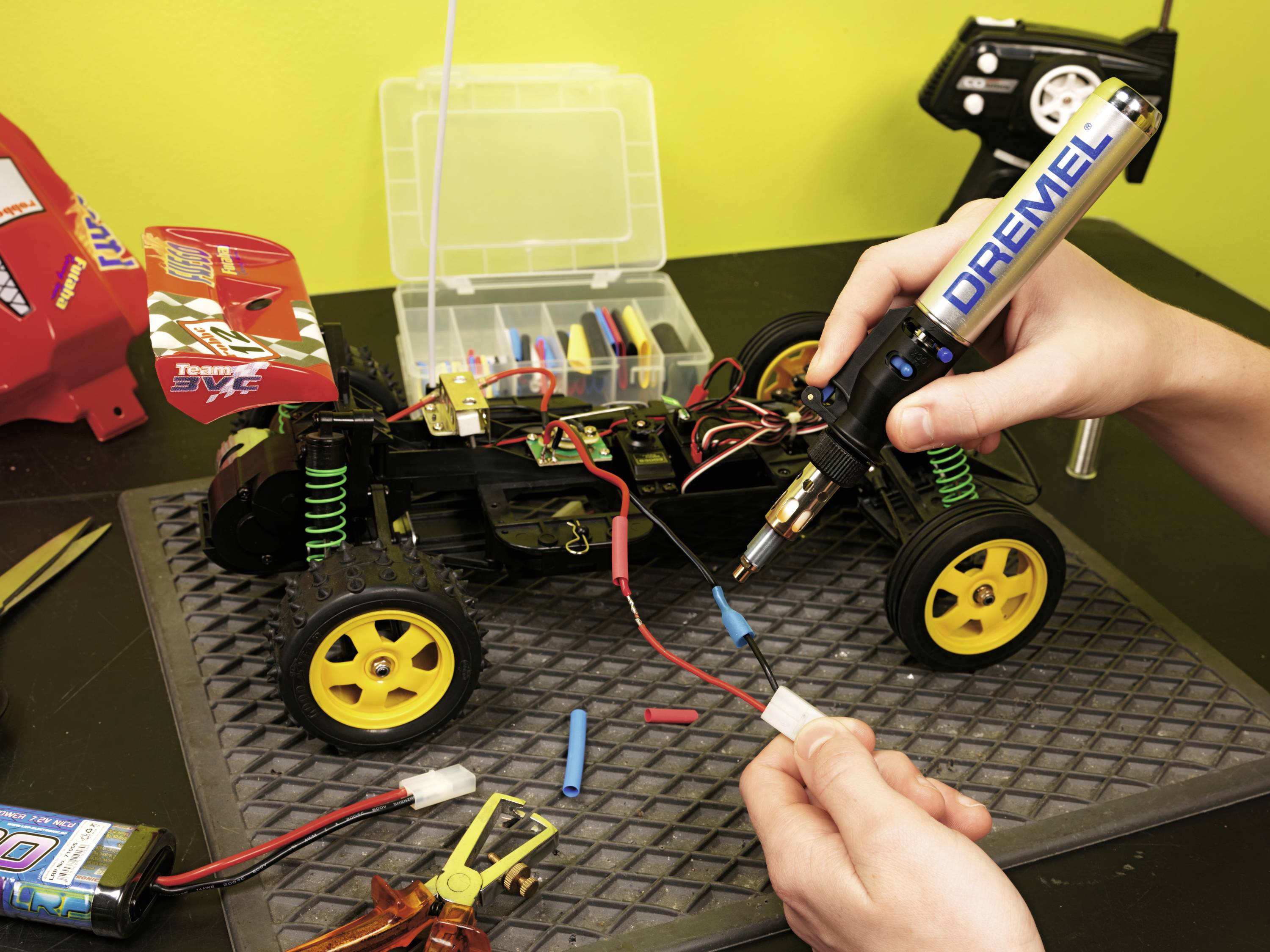A person is soldering wires on a remote-controlled car. Tools and an open toolbox are lying on the table.