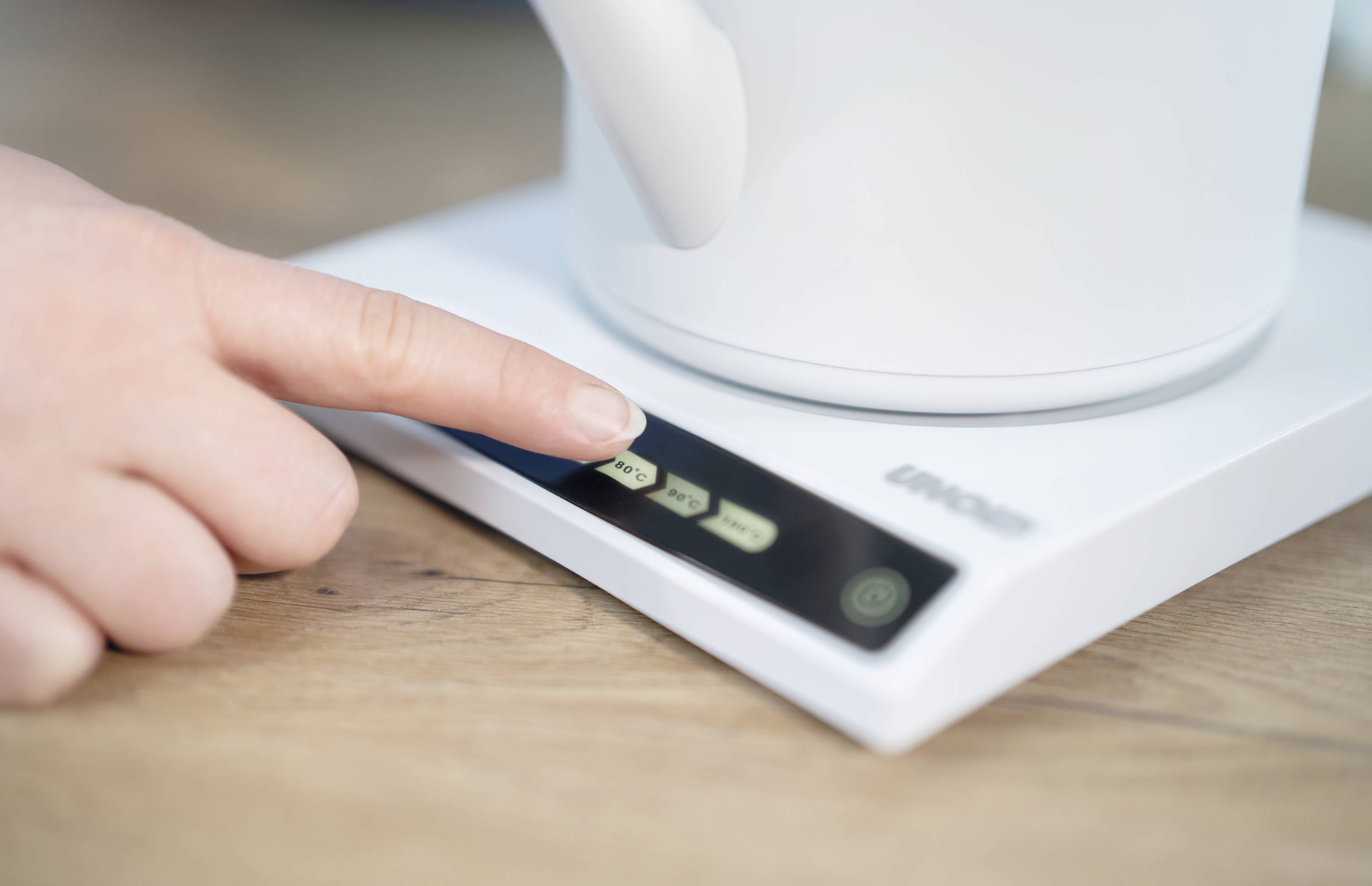 A finger presses the button on a digital control panel of a kitchen appliance, likely for setting or activation.