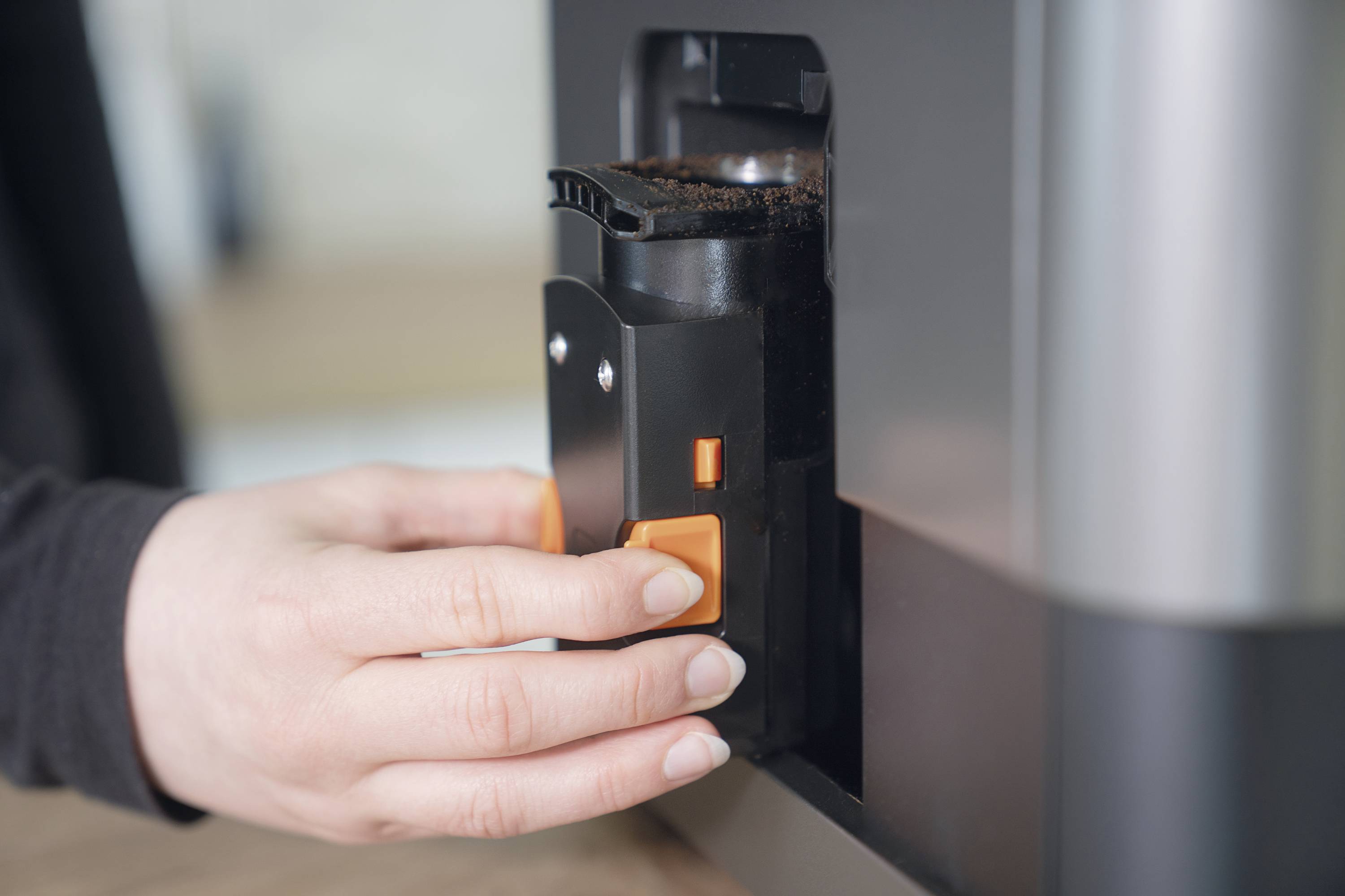 Person holding a coffee bean container at a coffee machine, showing the process of removing or inserting the container.