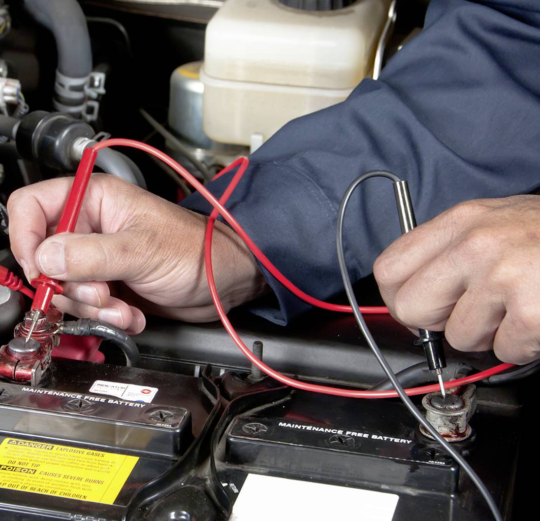 A person measures the voltage of a car battery by placing the test probes on the battery terminals.