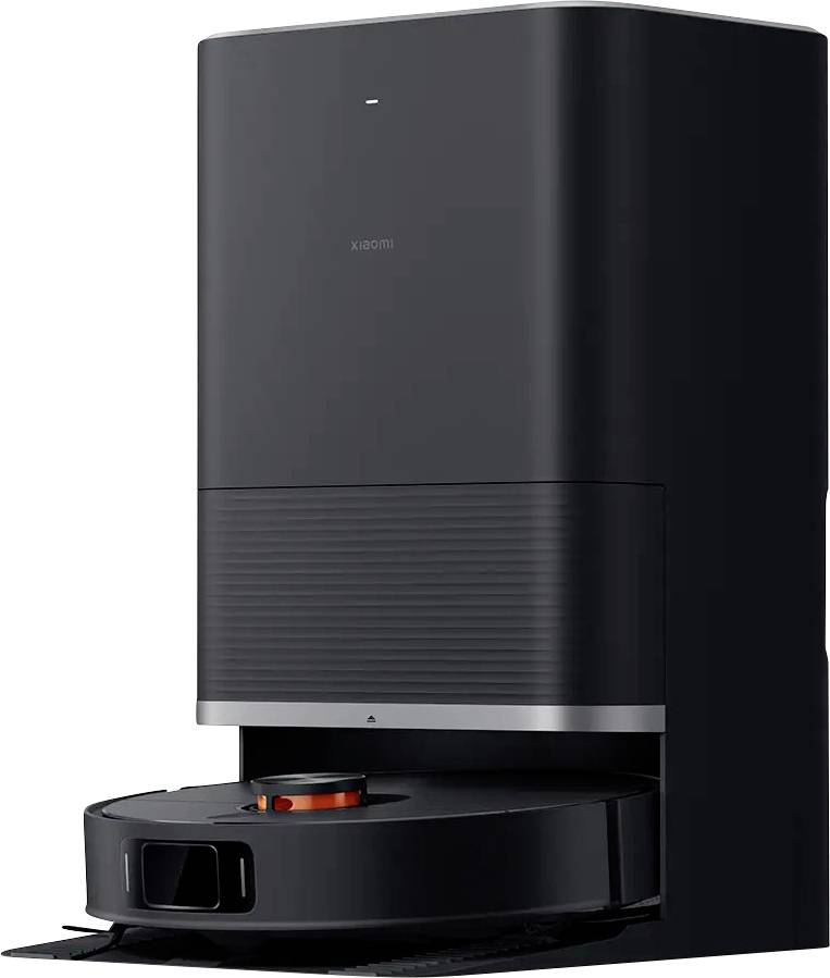 A black robotic vacuum cleaner in a charging station. The robot has an orange marking on its top surface and is ready for cleaning.