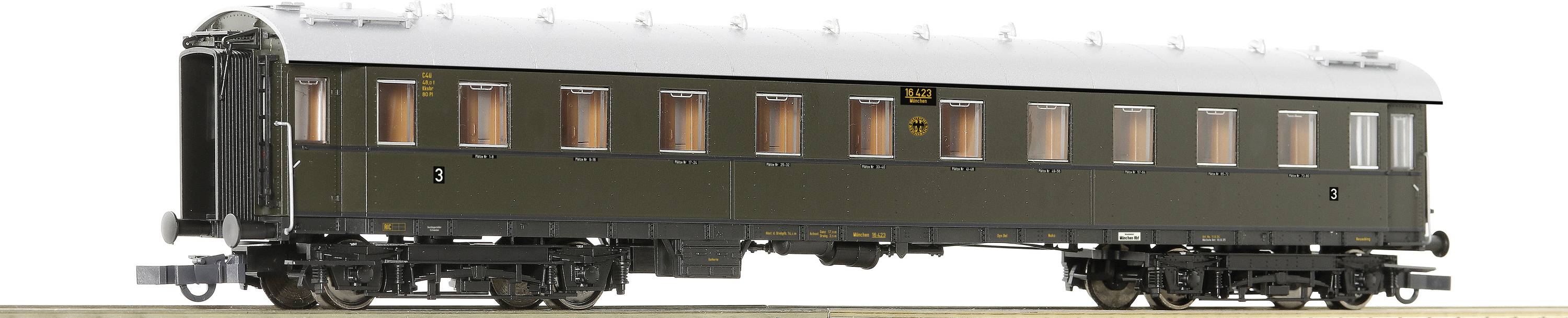 A dark green, historic railway passenger carriage with multiple windows. The carriage is standing on tracks and has a white roof.