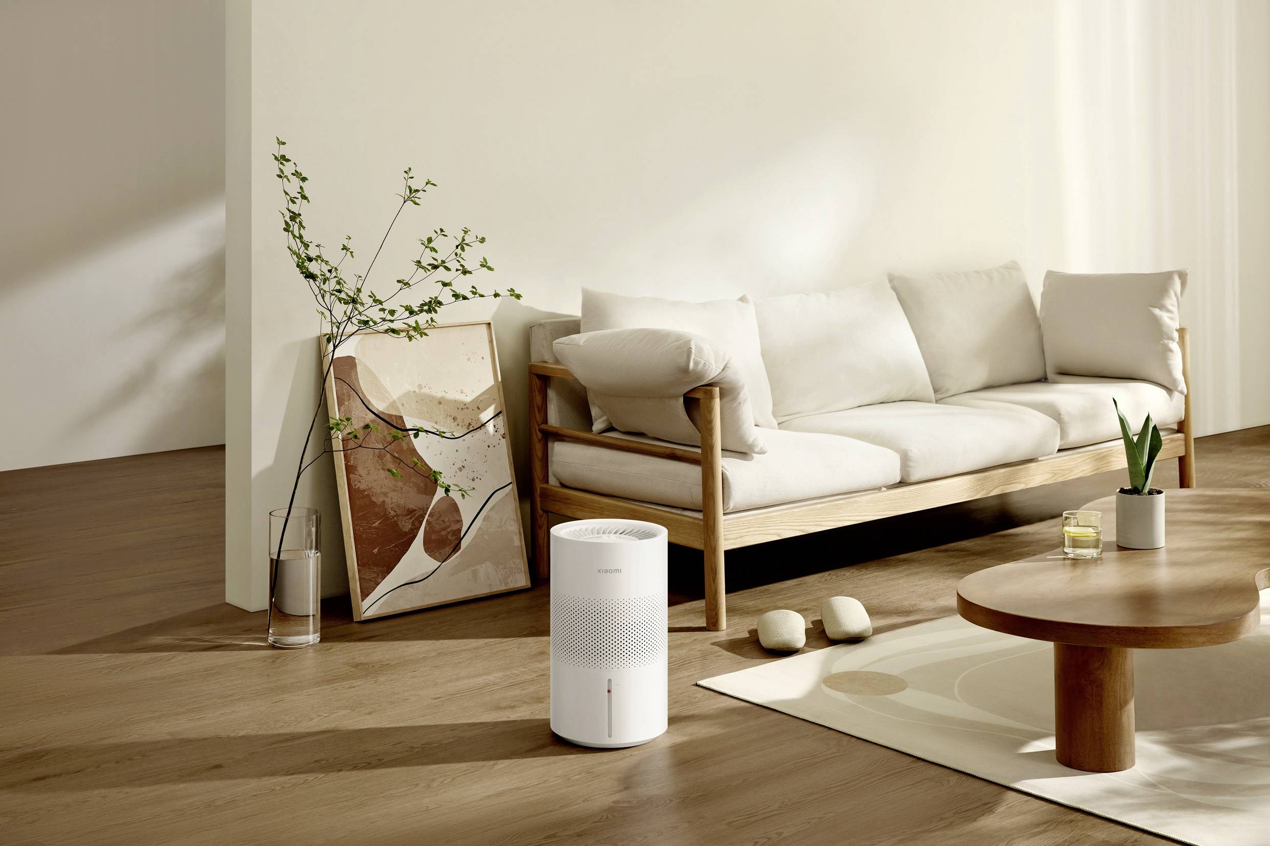 A bright living room with a cream-coloured sofa, a white air purifier, a wooden table and a plant, the atmosphere is minimalist.