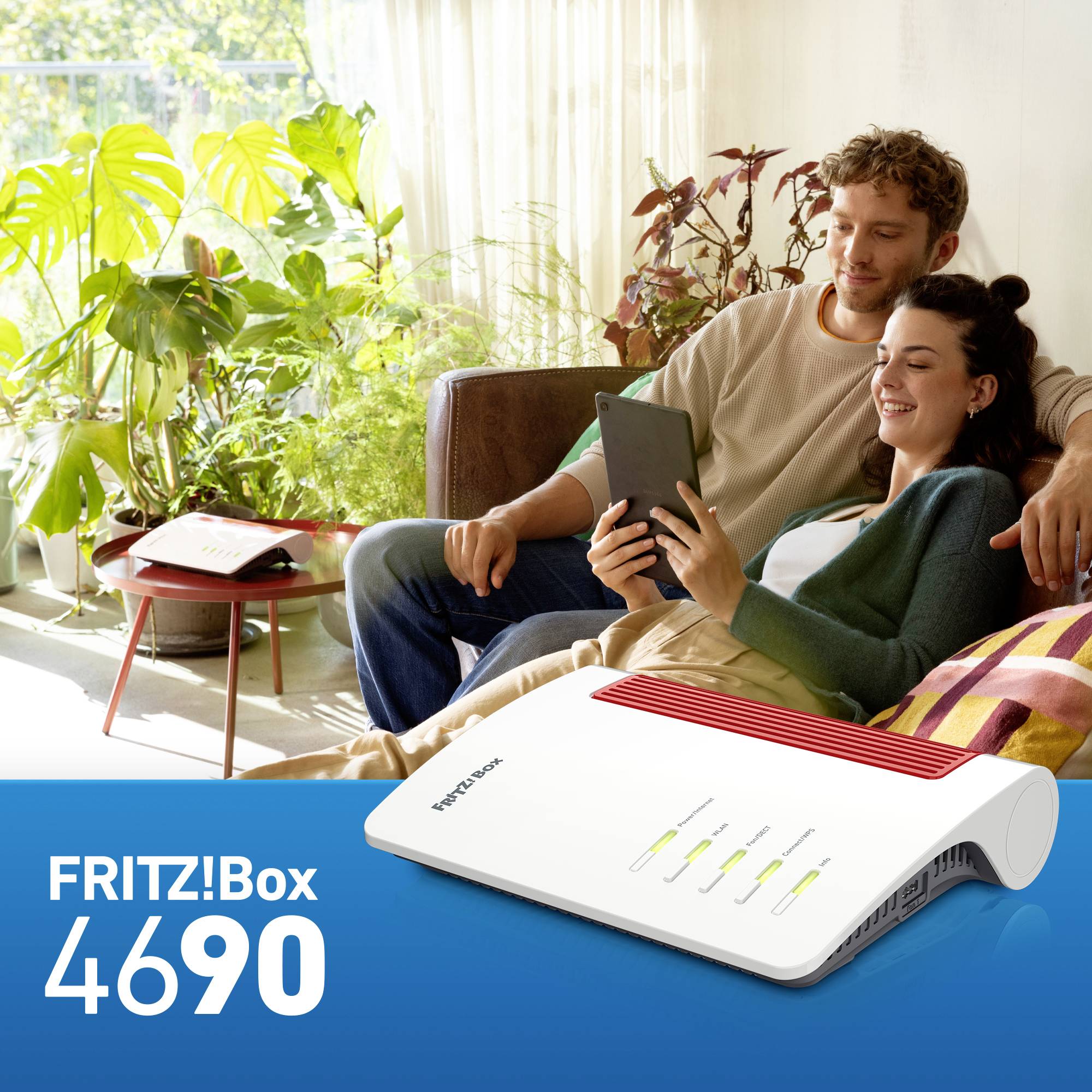 A smiling couple sits on a sofa and uses a tablet. A FRITZ!Box 4690 router is pictured in the foreground.