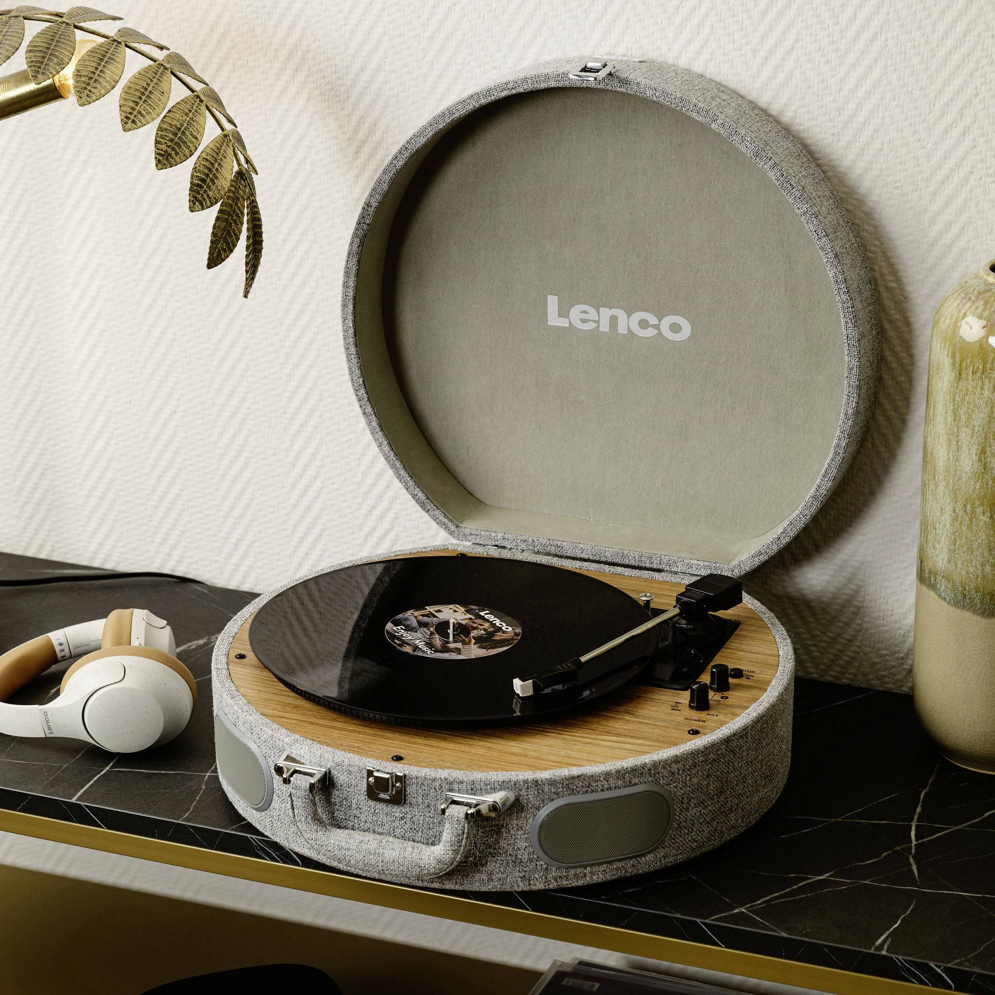 A record player by the brand 'Lenco' with an open lid plays a vinyl record. A pair of headphones lies next to the turntable.