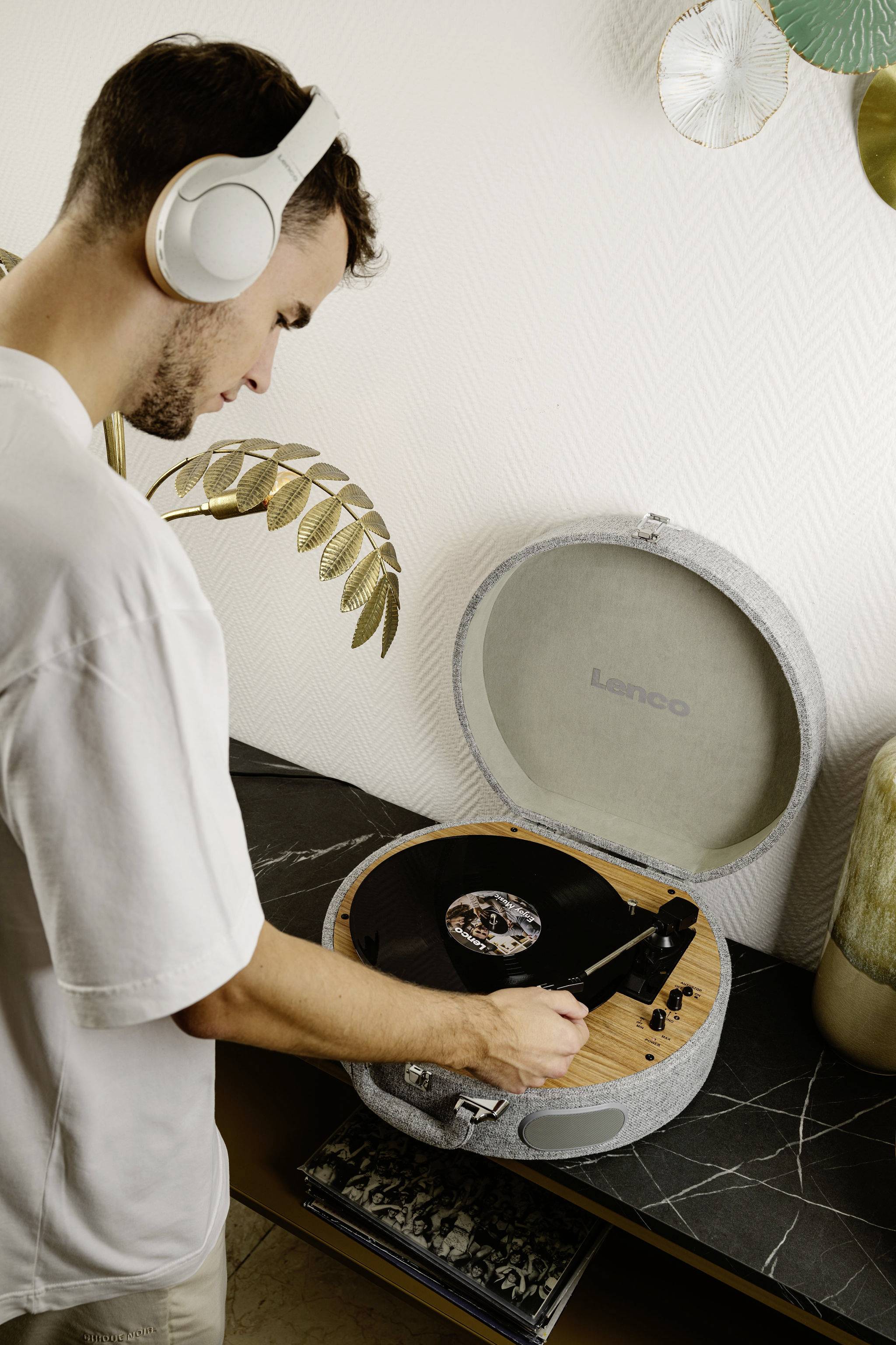 A man wearing headphones places a vinyl record on a turntable in a modern room.