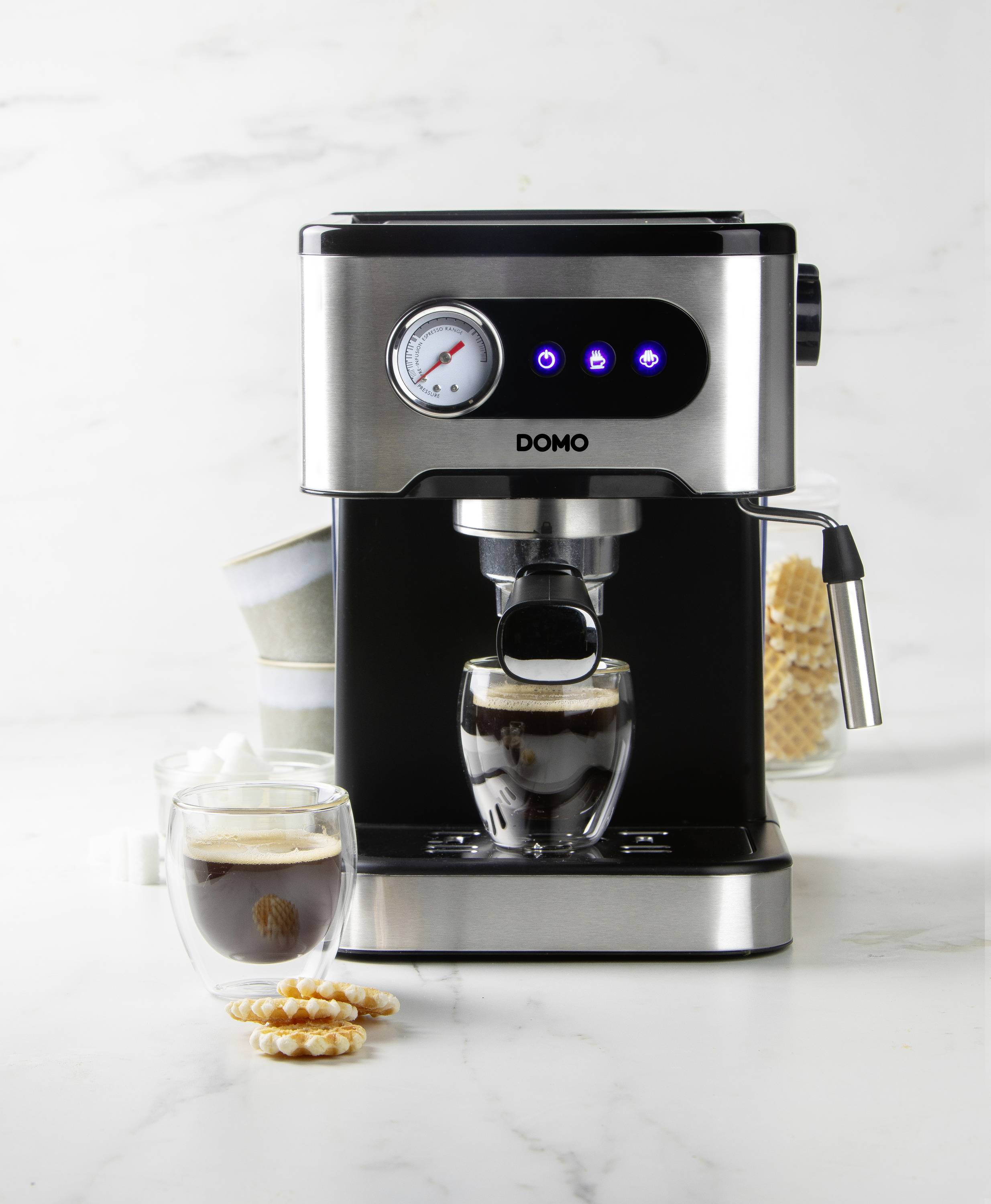 Espresso machine with two glasses of espresso in front, stacked cups and sugar in the background; surrounded by modern, elegant kitchen appliances.