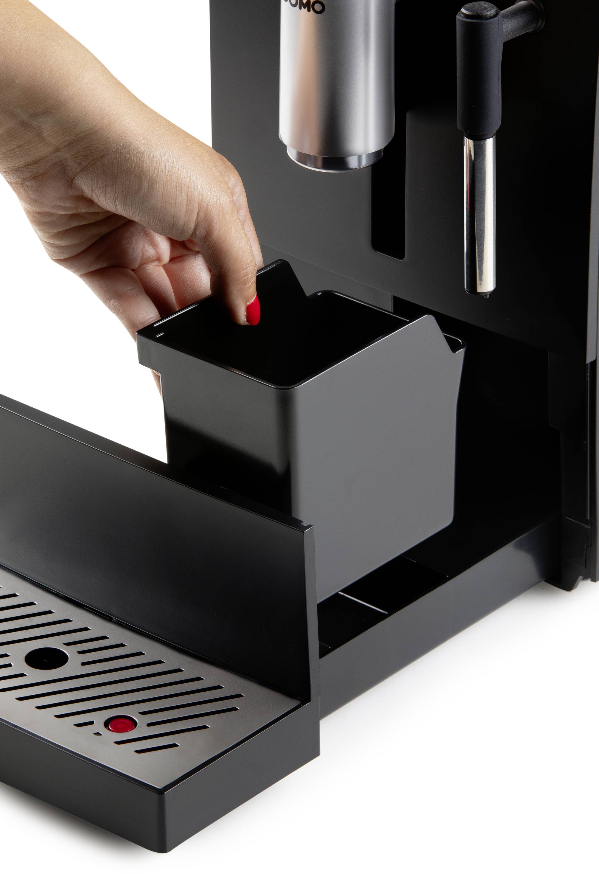 A hand removes a rectangular container from a coffee machine. The container is likely used for disposing of used coffee grounds.