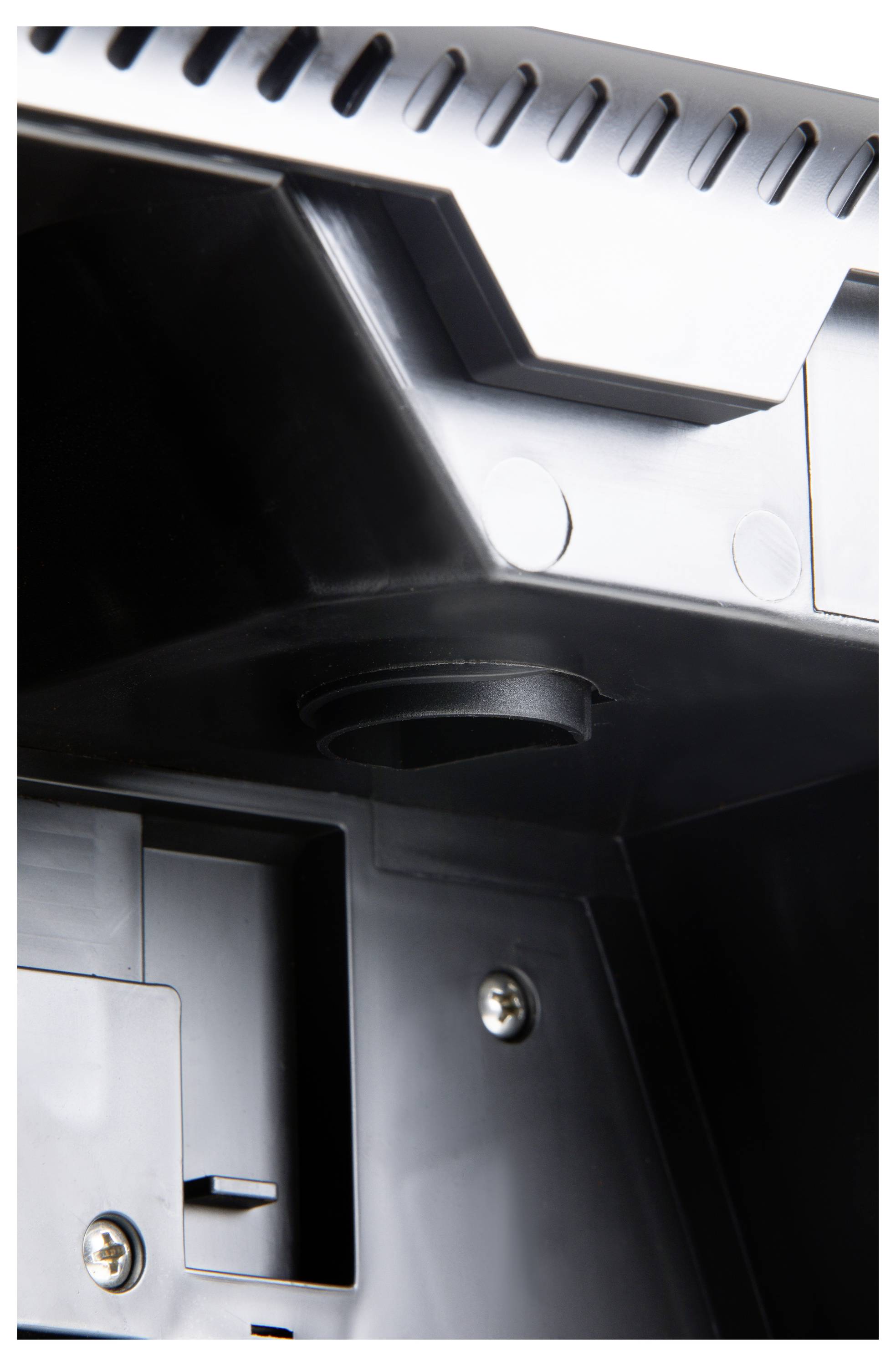 Close-up of part of an electronic device, with screws and a circular connection, surrounded by black plastic.