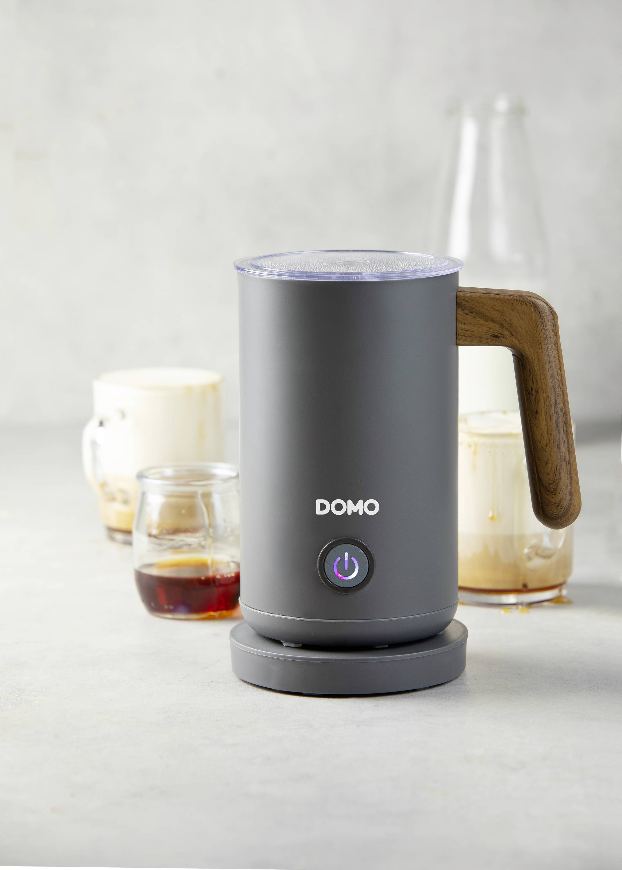 Electric milk frother with wooden handle, surrounded by glasses of coffee and milk foam. Perfect for coffee preparation.