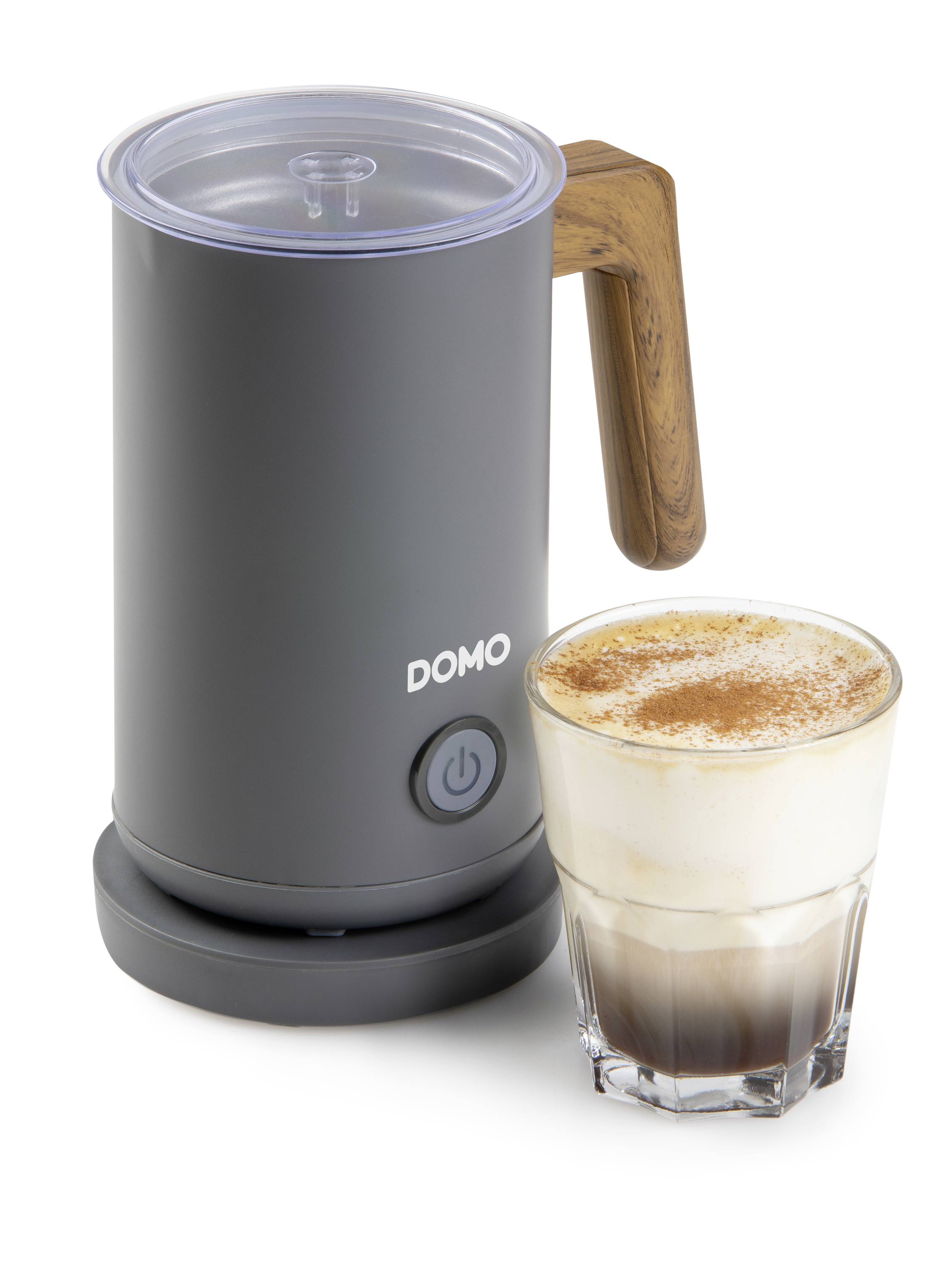 An electric milk frother next to a glass of latte macchiato topped with milk foam and dusted with cocoa powder.