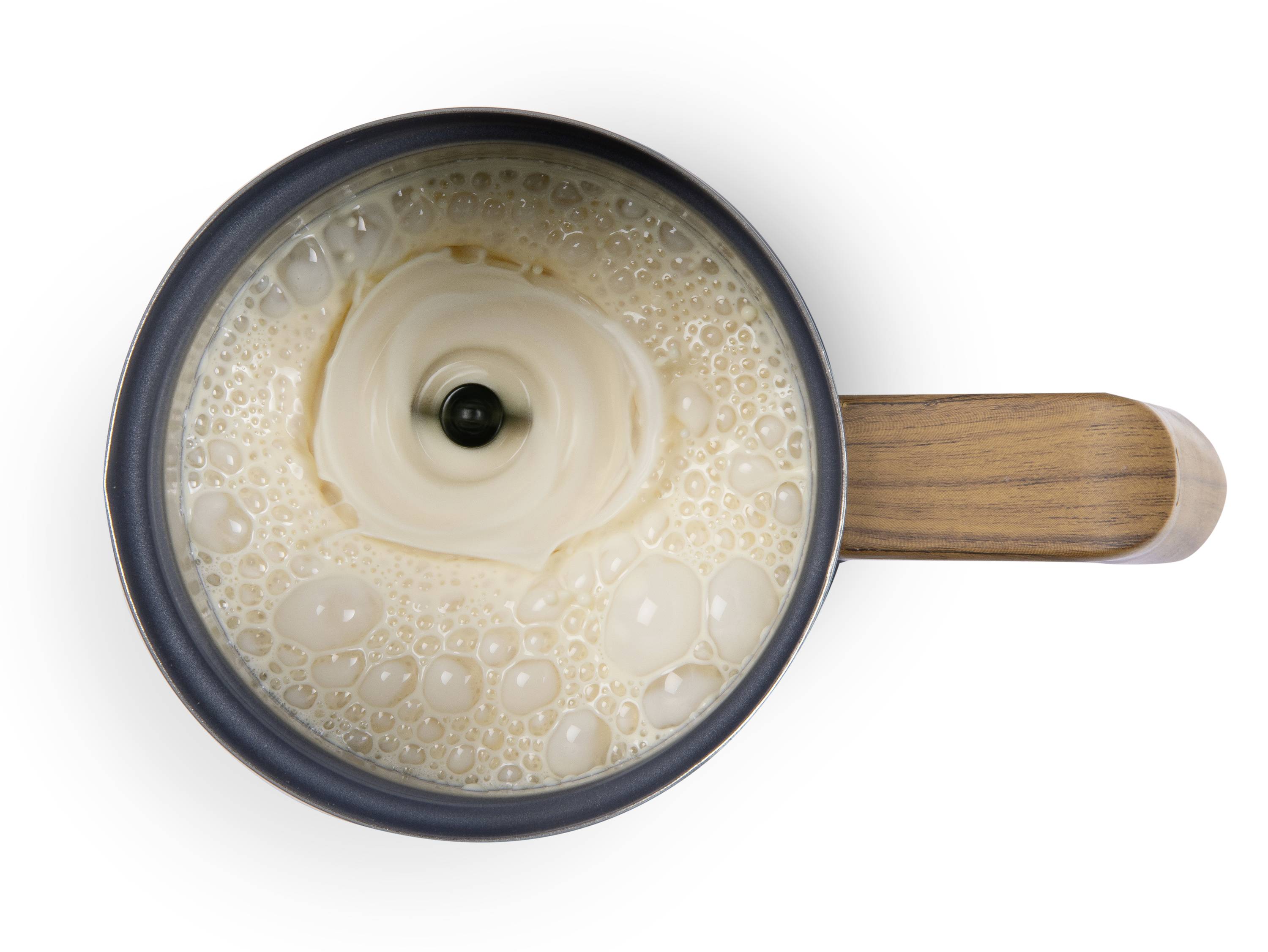 Top-down view of a cup with coffee being poured into the centre of a milk wave pattern. Wooden handle visible on the right.