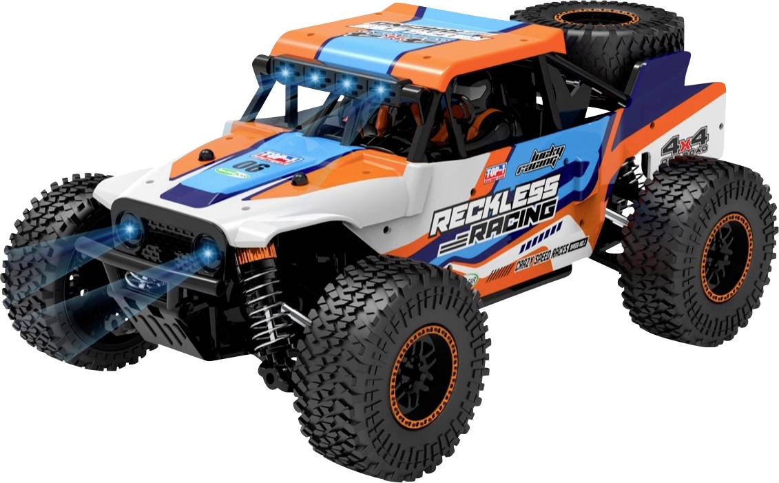 A remote-controlled off-road style car, primarily in white, orange, and blue. Large wheels, lighting, and 'Reckless Racing' inscription.