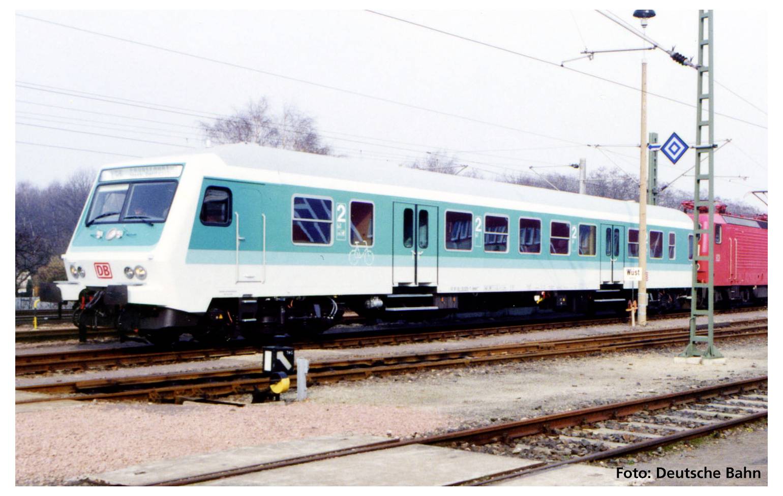 A green and white train is standing on a railway track. It is a Deutsche Bahn train, surrounded by power lines and railway infrastructure.