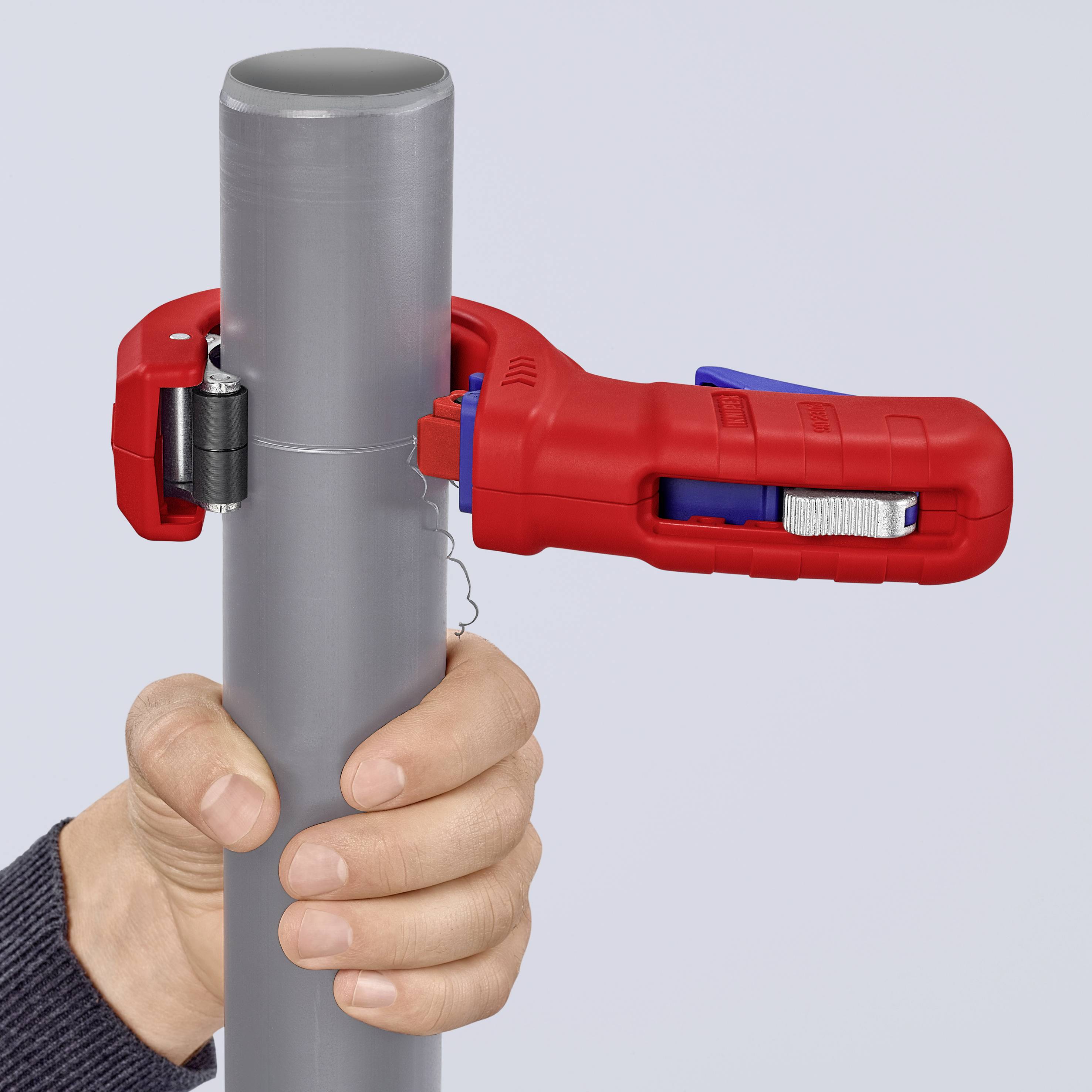 A hand is holding a grey pipe with a red pipe cutter. The pipe cutter is fastened around the pipe and ready to cut.