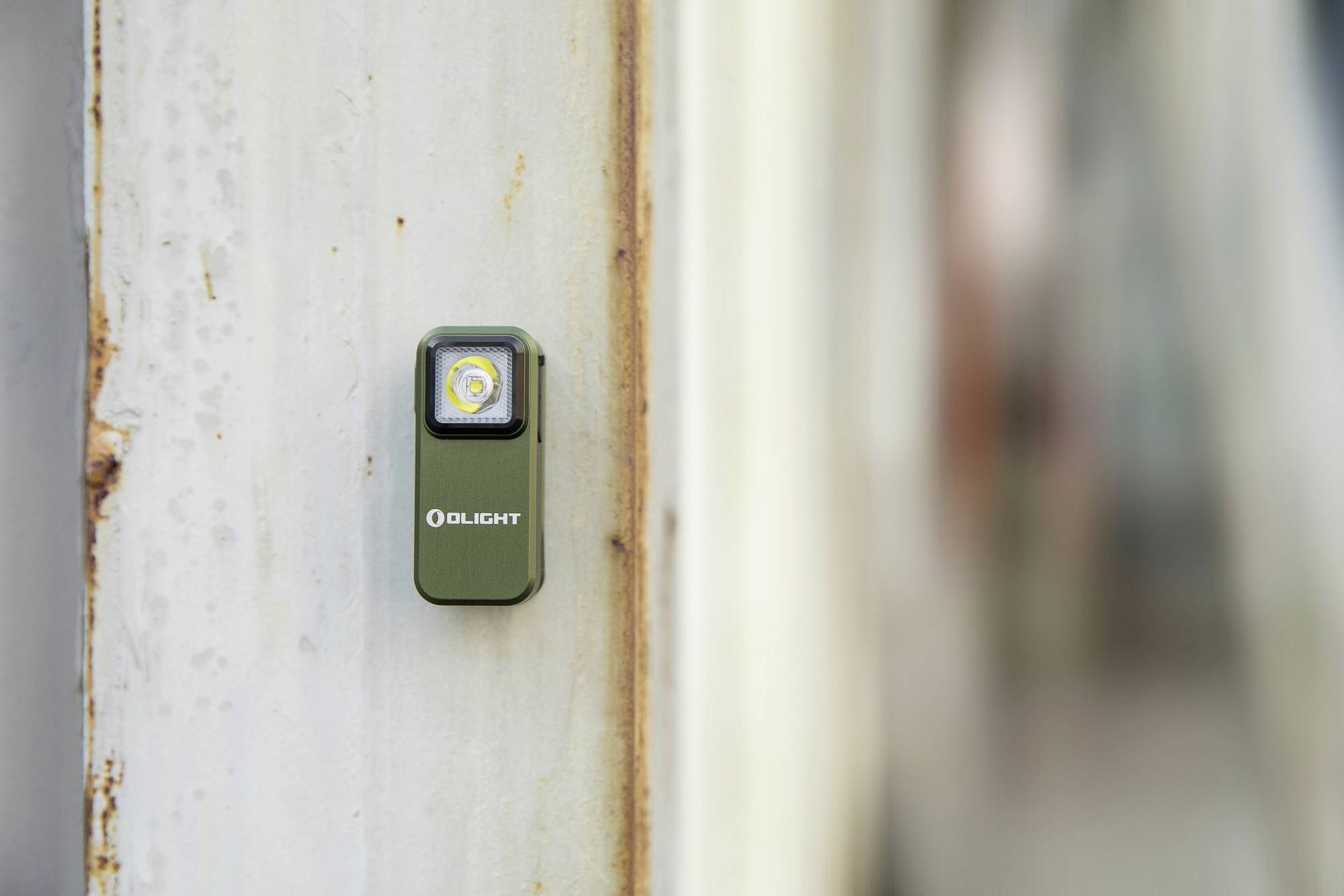 A small, green LED torch is attached to a metallic, slightly rusty surface.
