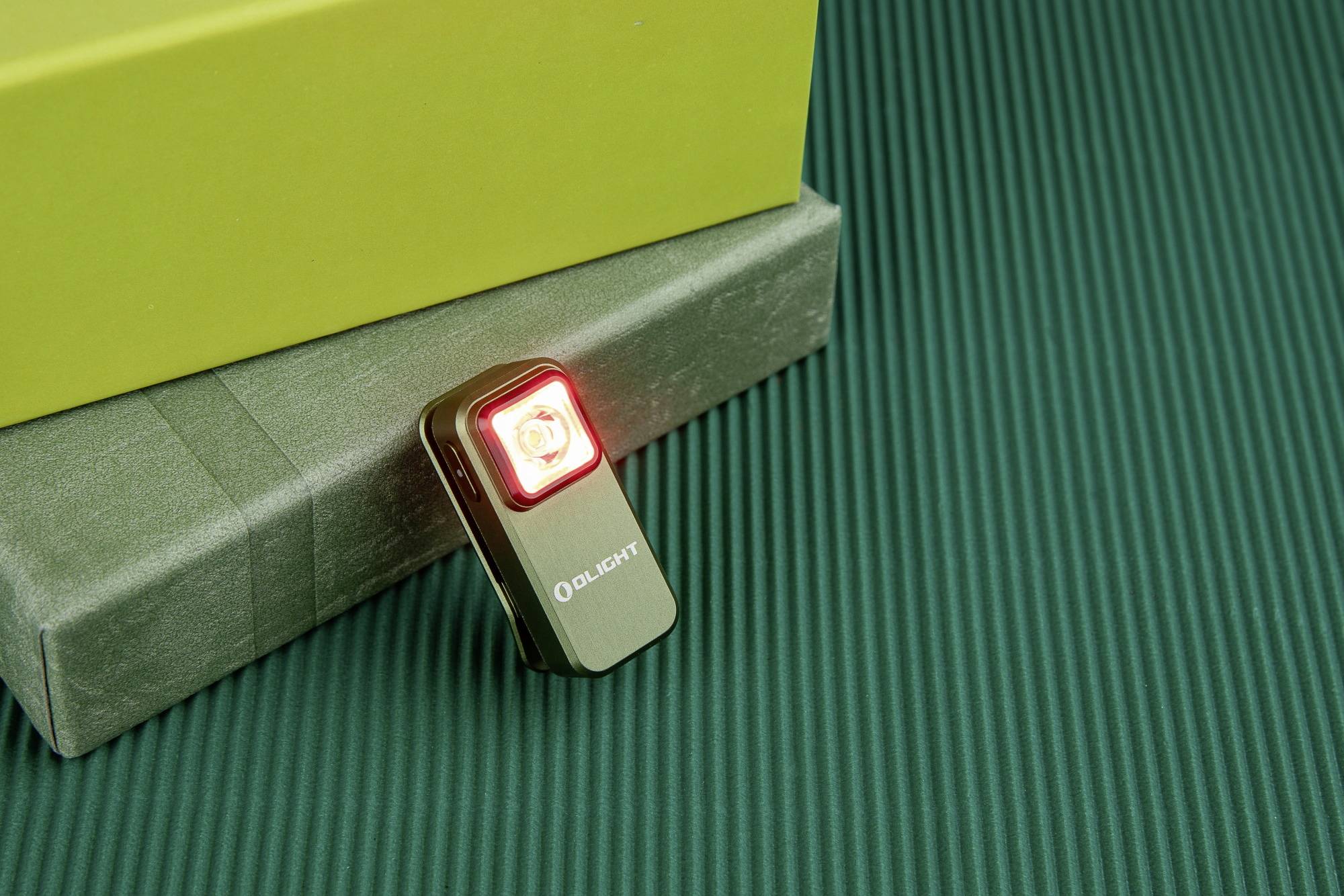 A small black torch with a red light illuminates on a green, ribbed surface next to a yellow box.